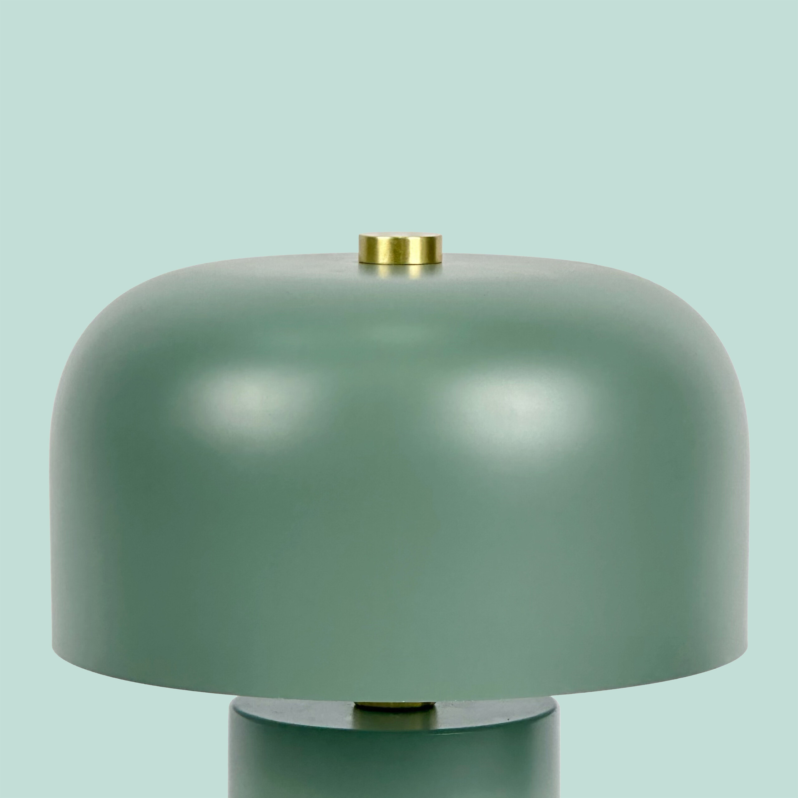 Eine moderne grüne Pilz-Tischlampe mit goldenem Knauf vor hellgrünem Hintergrund.