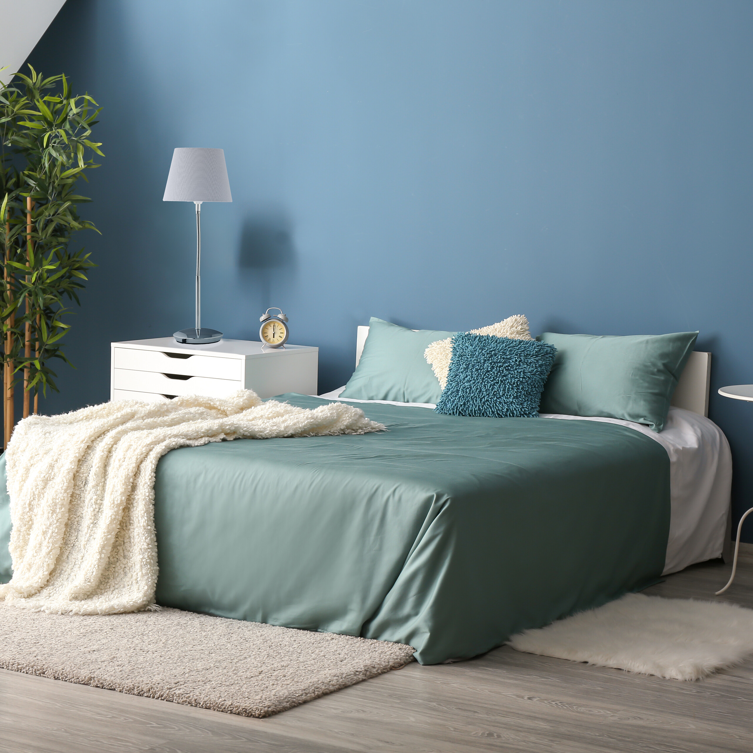Gemütliches Schlafzimmer mit blauem Bett, wei ßem Nachtisch, Lampe und grüner Wand vor einem Holzboden.