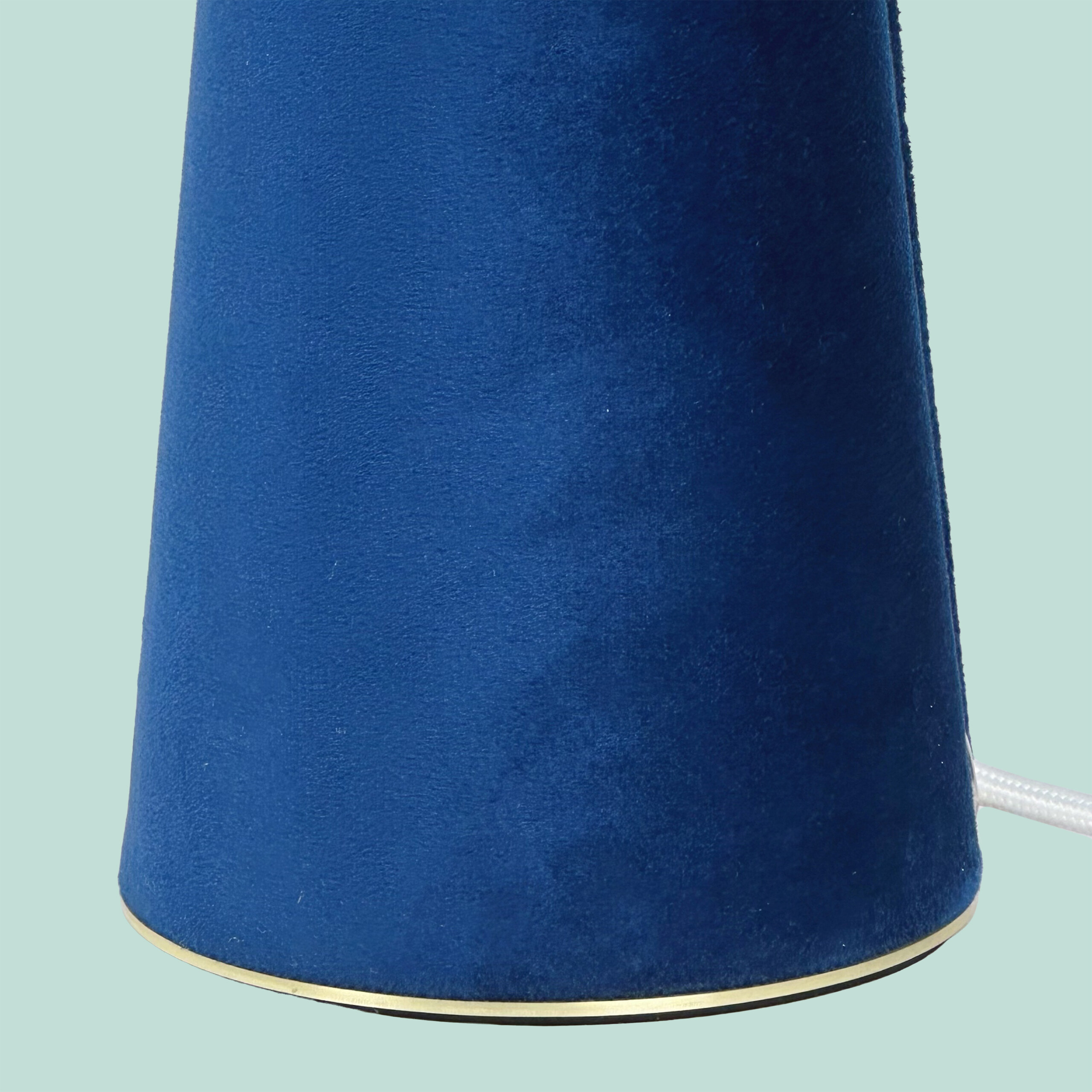 Ein blauer kegelförmiger Lampenschirm mit goldenem Rand auf hellblauem Hintergrund.