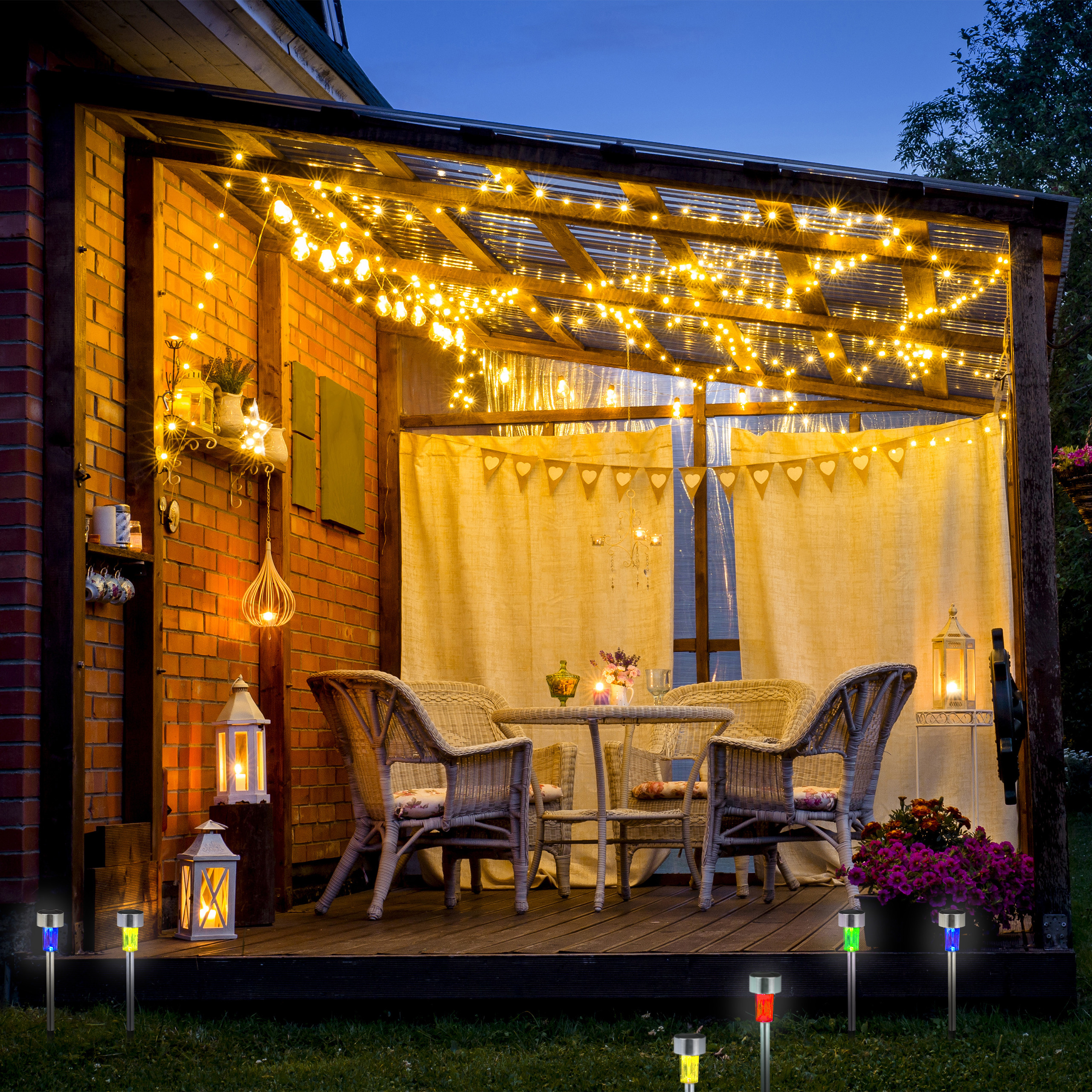 Beleuchtete Holzterrasse mit Rattansesseln, Tisch und Lichterketten bei Nacht.