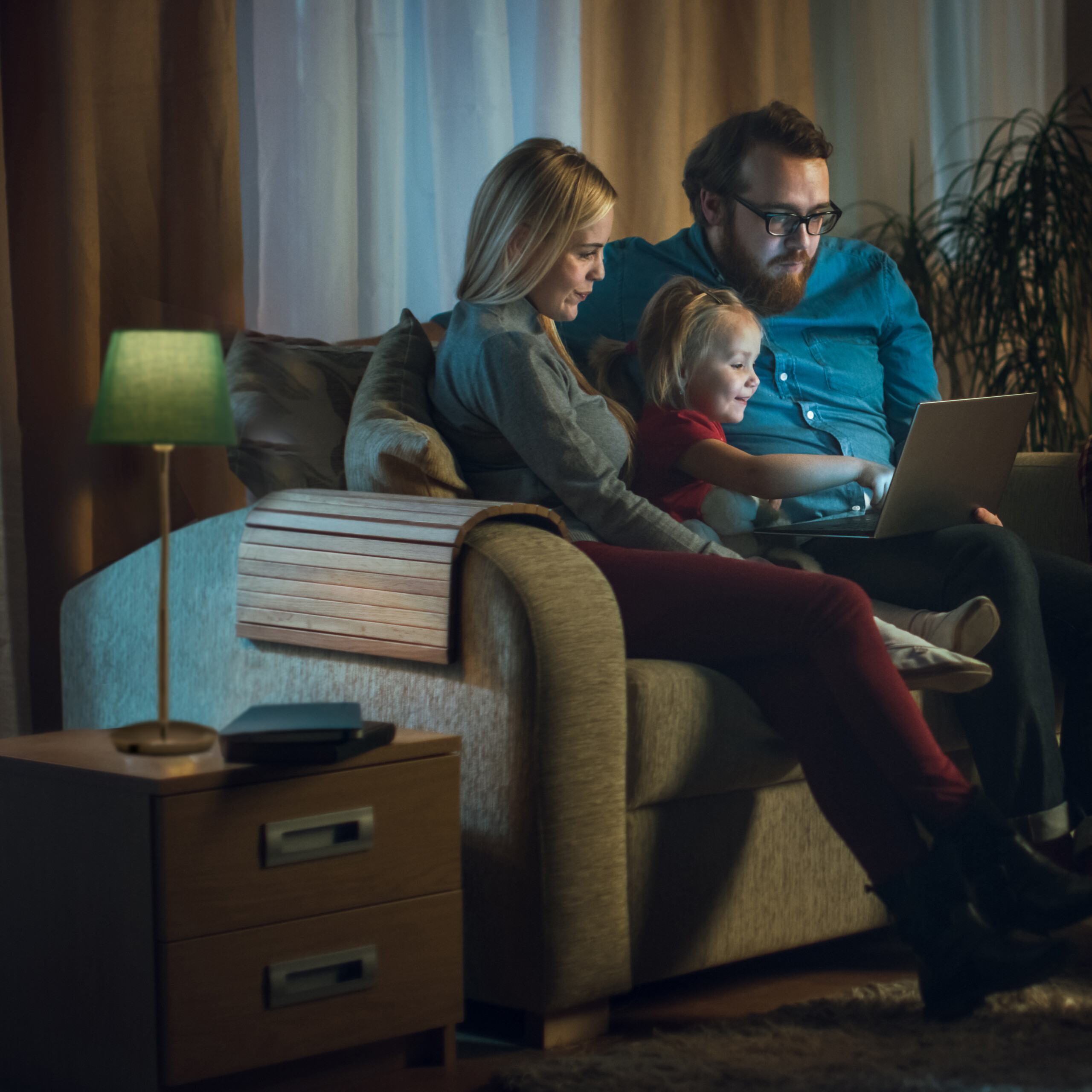 Eine Familie sitzt auf einem Sofa und schaut abends gemeinsam in einen Laptop.