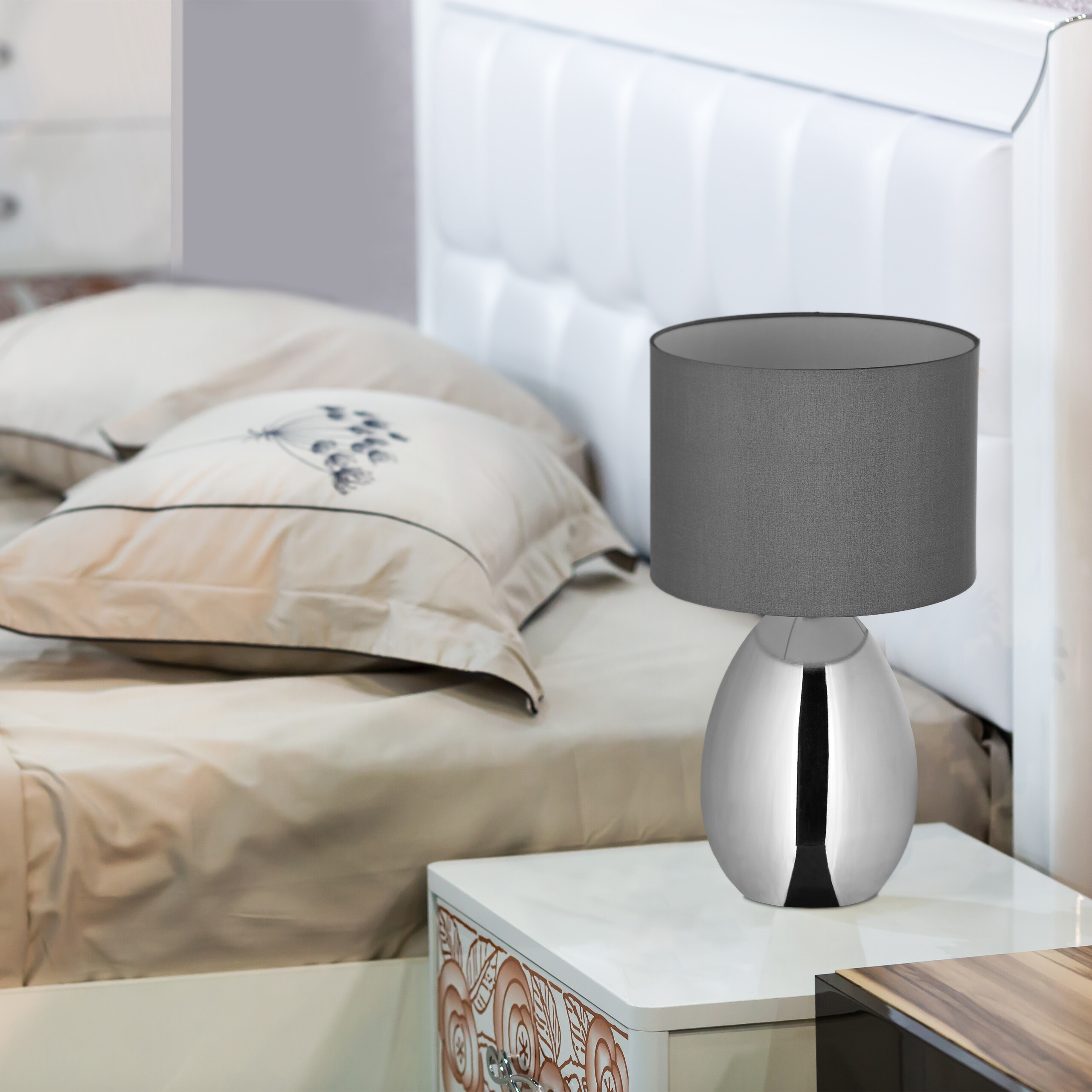 Eine moderne Chrom-Tischlampe mit grauem Schirm steht auf einem Nachttisch.