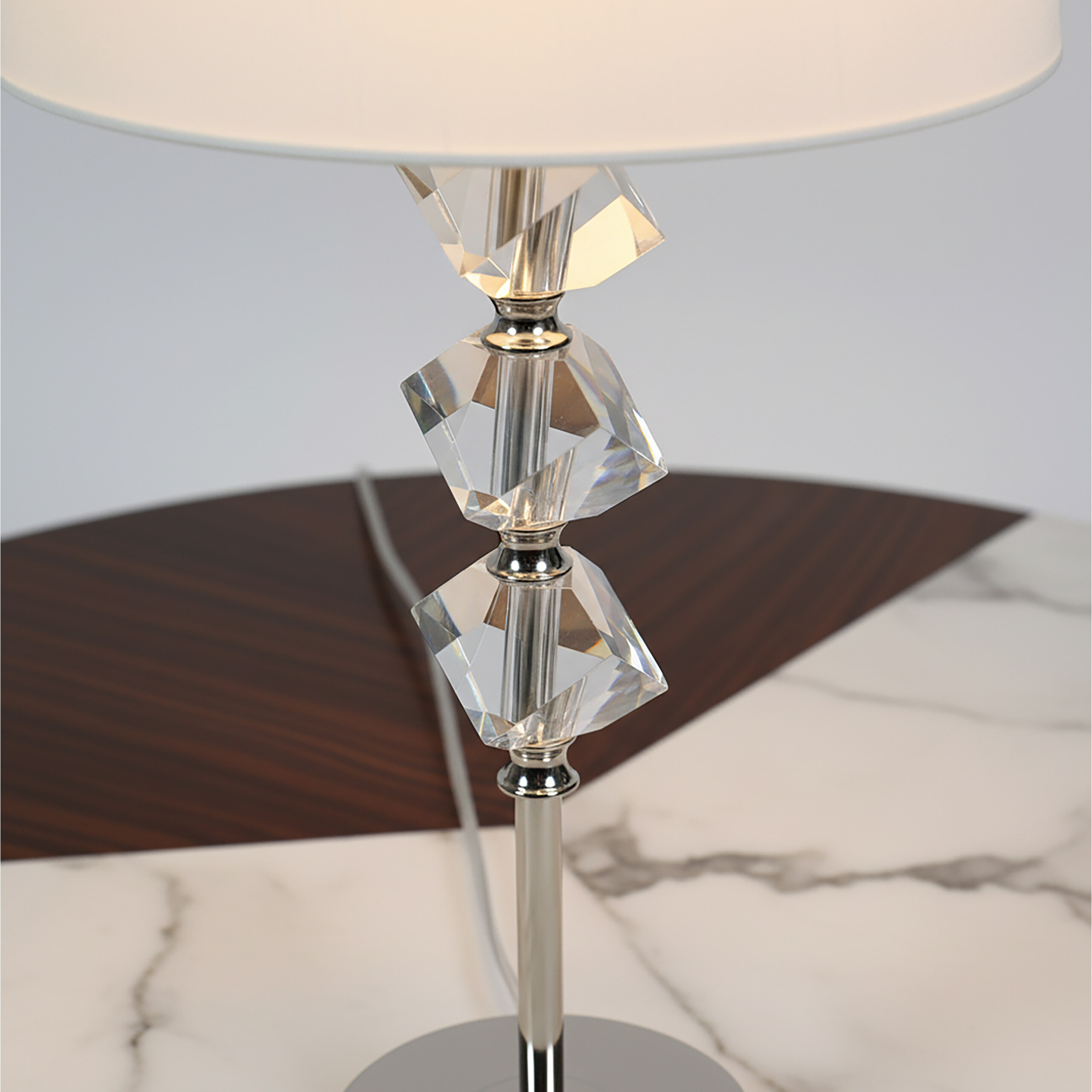 Eine Tischlampe mit weißem Schirm und gestapelten Kristallkugeln auf einem Marmor- und Holztisch.