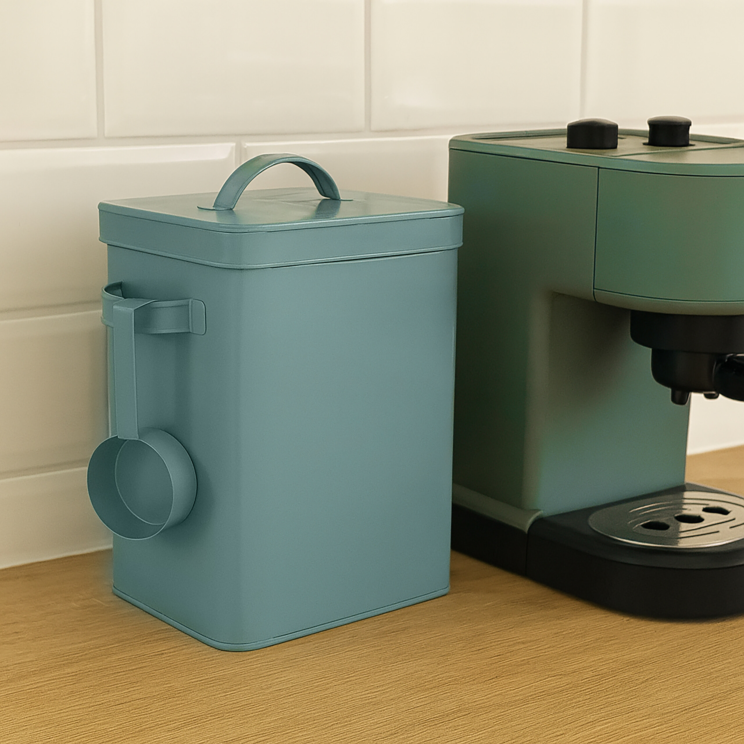 Ein blauer Vorratsbehälter mit Löffel und eine grüne Kaffeemaschine stehen auf einer Holzoberfläche vor weißen Fliesen.