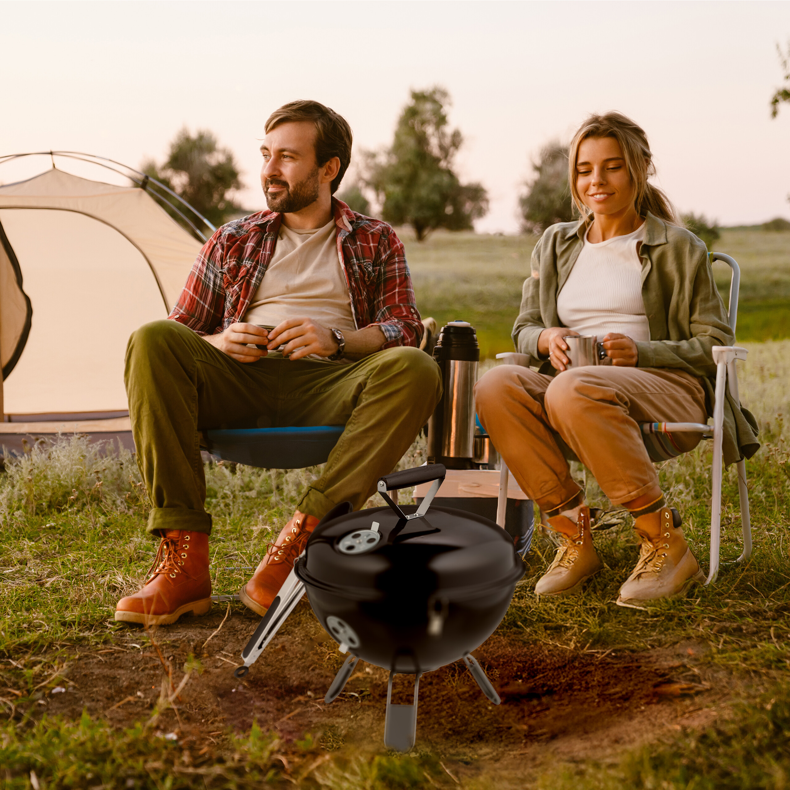 Ein Paar sitzt vor einem Zelt im Freien beim Camping, mit einem schwarzen Grill im Vordergrund.