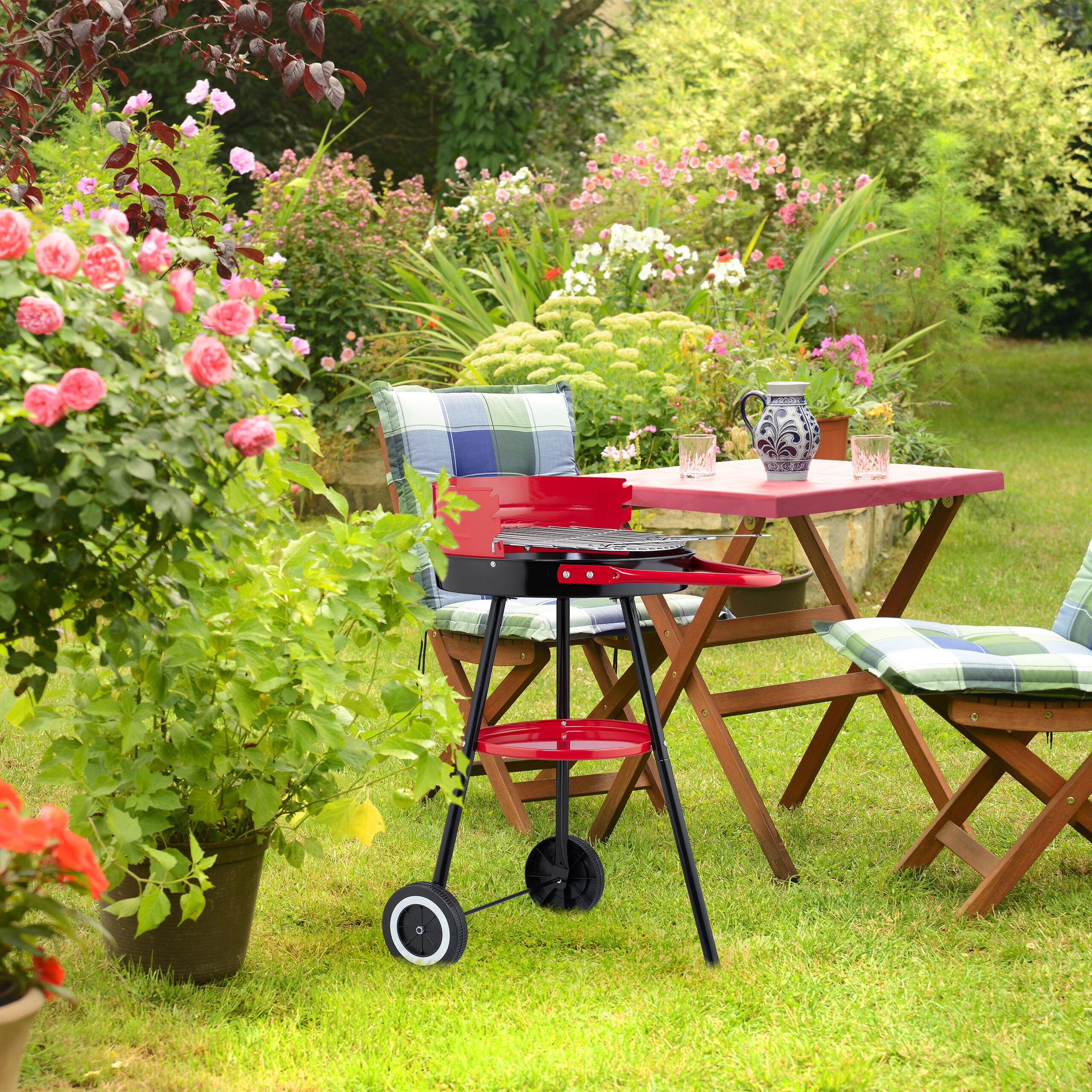 Ein roter Kugelgrill auf dem Rasen, im Hintergrund ein Holztisch mit Stühlen und ein blühender Garten.