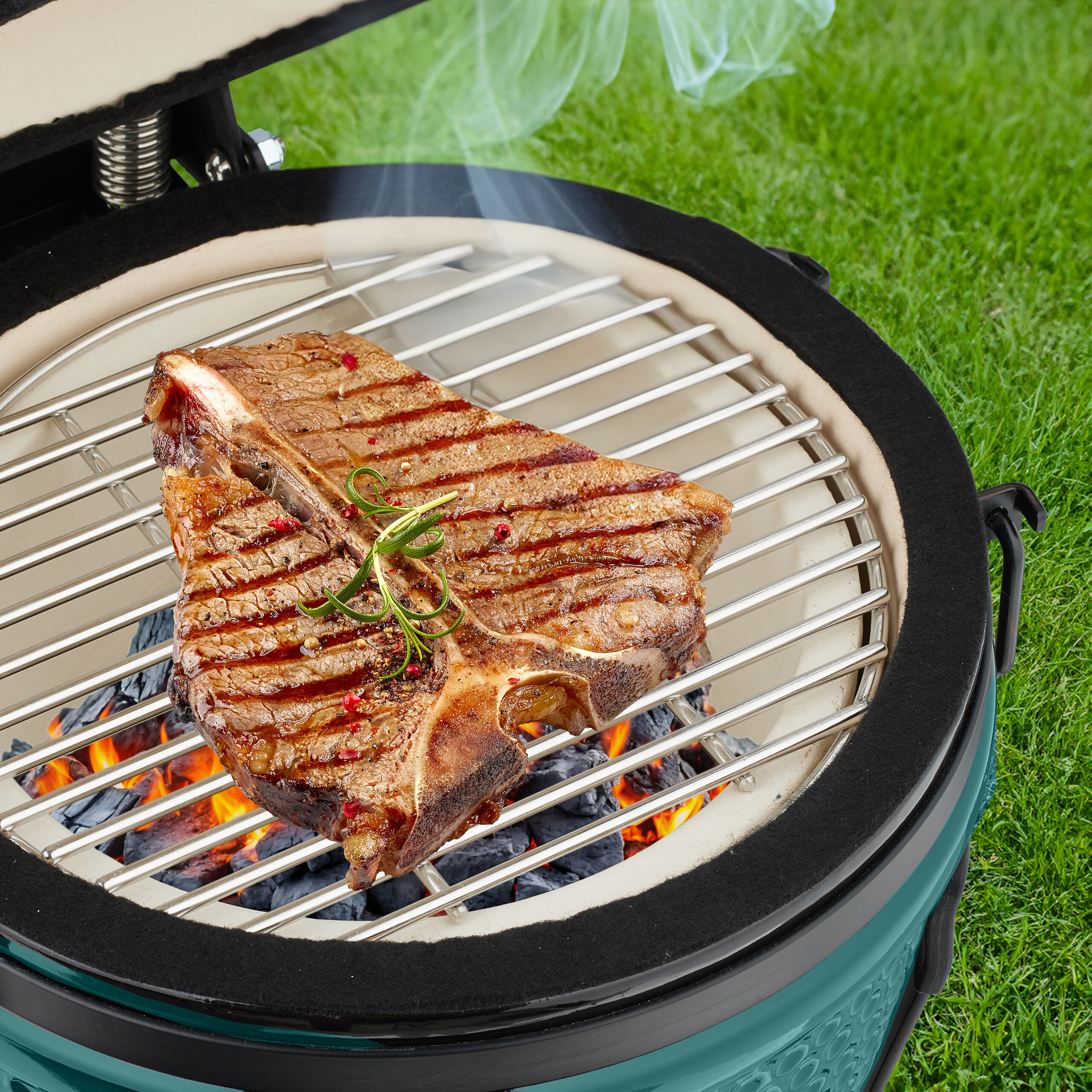 Ein saftiges T-Bone-Steak mit Kräutern grillt über Holzkohle auf einem runden Grill im Freien.