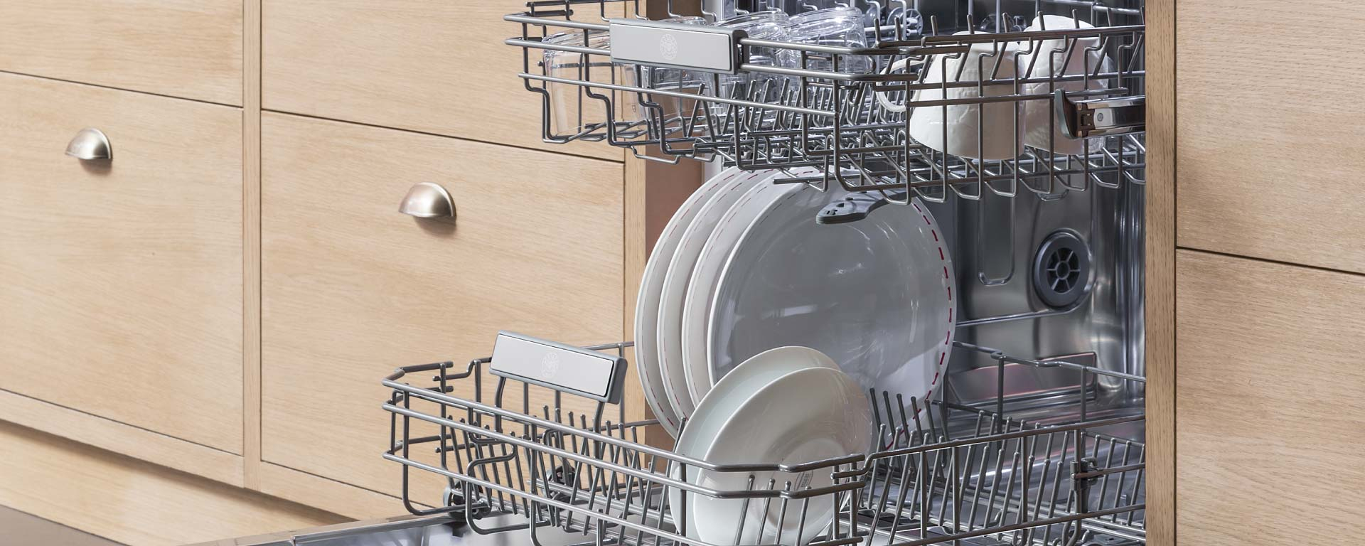 Una lavastoviglie aperta in una cucina in legno, caricata con piatti e bicchieri puliti.