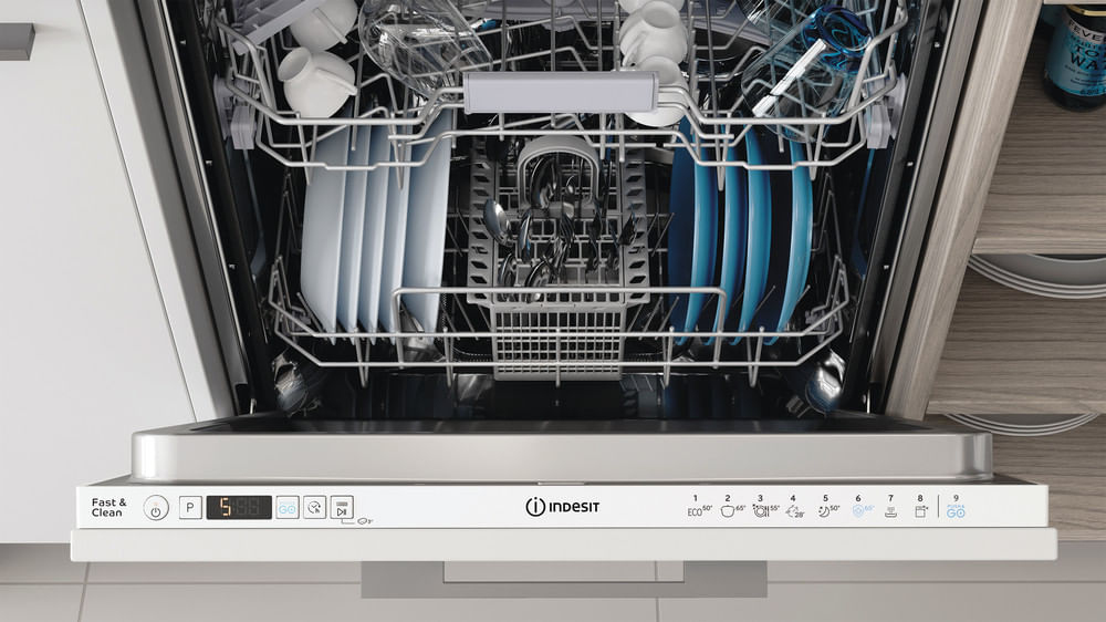 Una lavastoviglie Indesit aperta con piatti, tazze, bicchieri e un cestello per posate puliti.