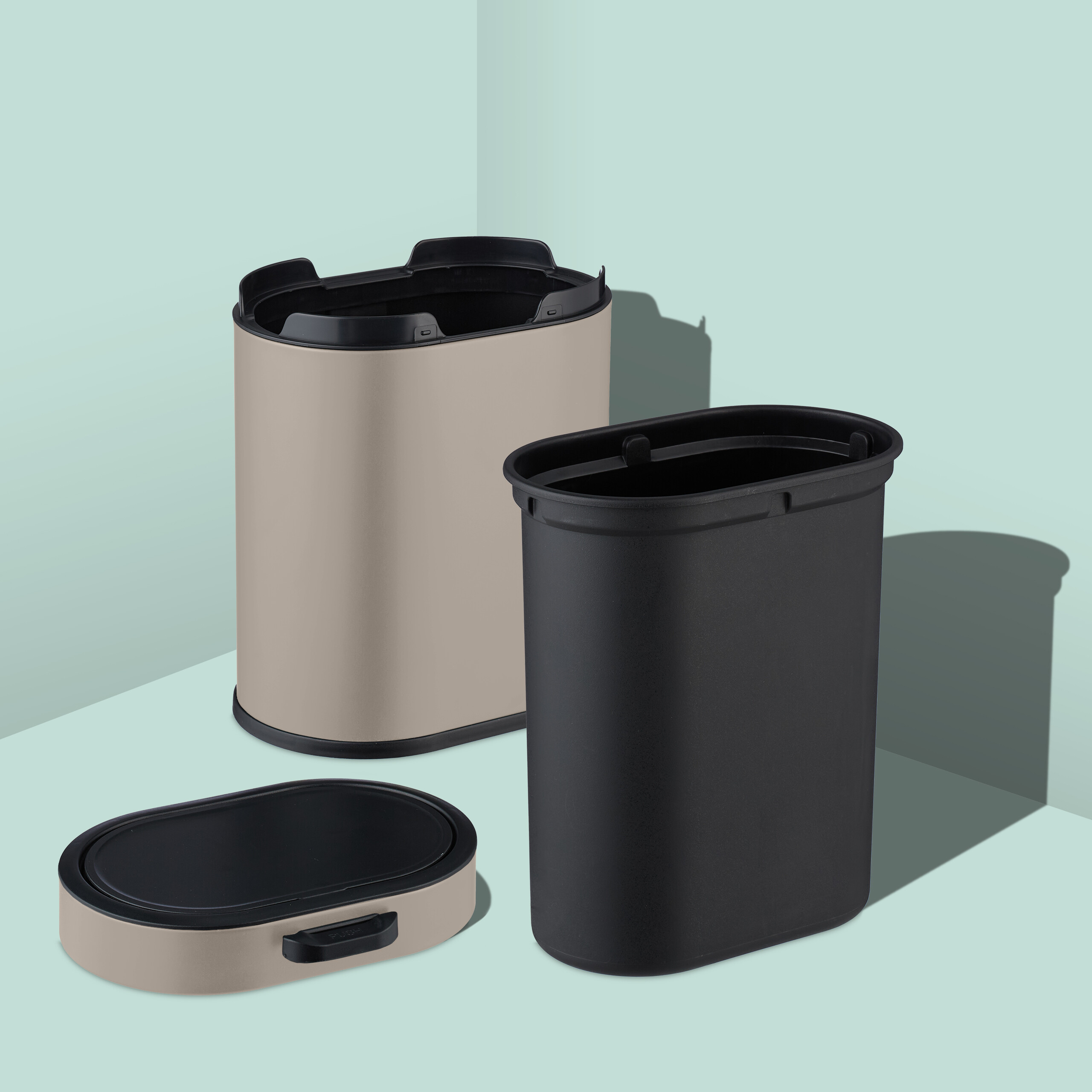 Beige und schwarze ovale Mülleimer mit Inneneimer und Push-Deckel vor einer mintgrünen Wand.