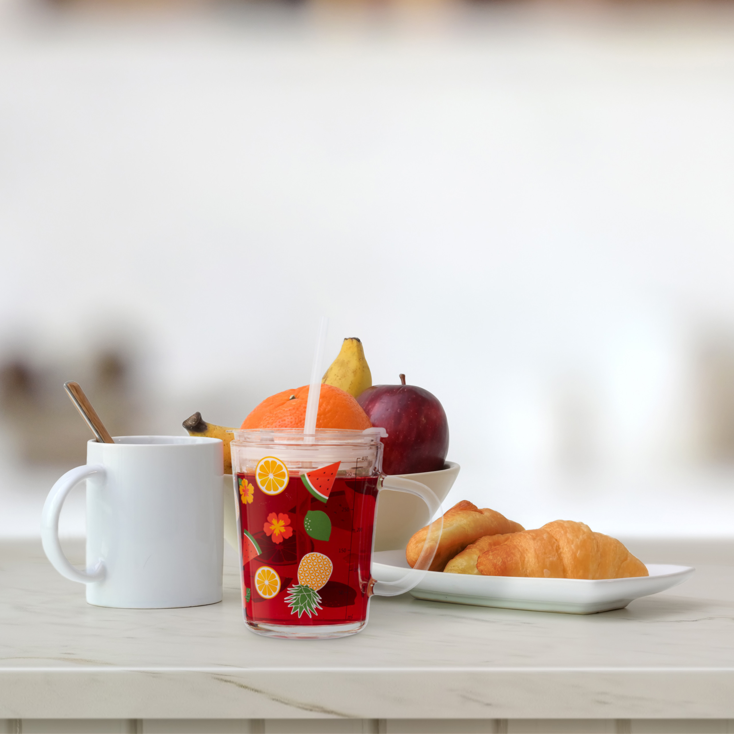 Frühstückstisch mit Tasse, Fruchtgetränk, Obstschale und zwei Croissants auf einer weißen Platte.