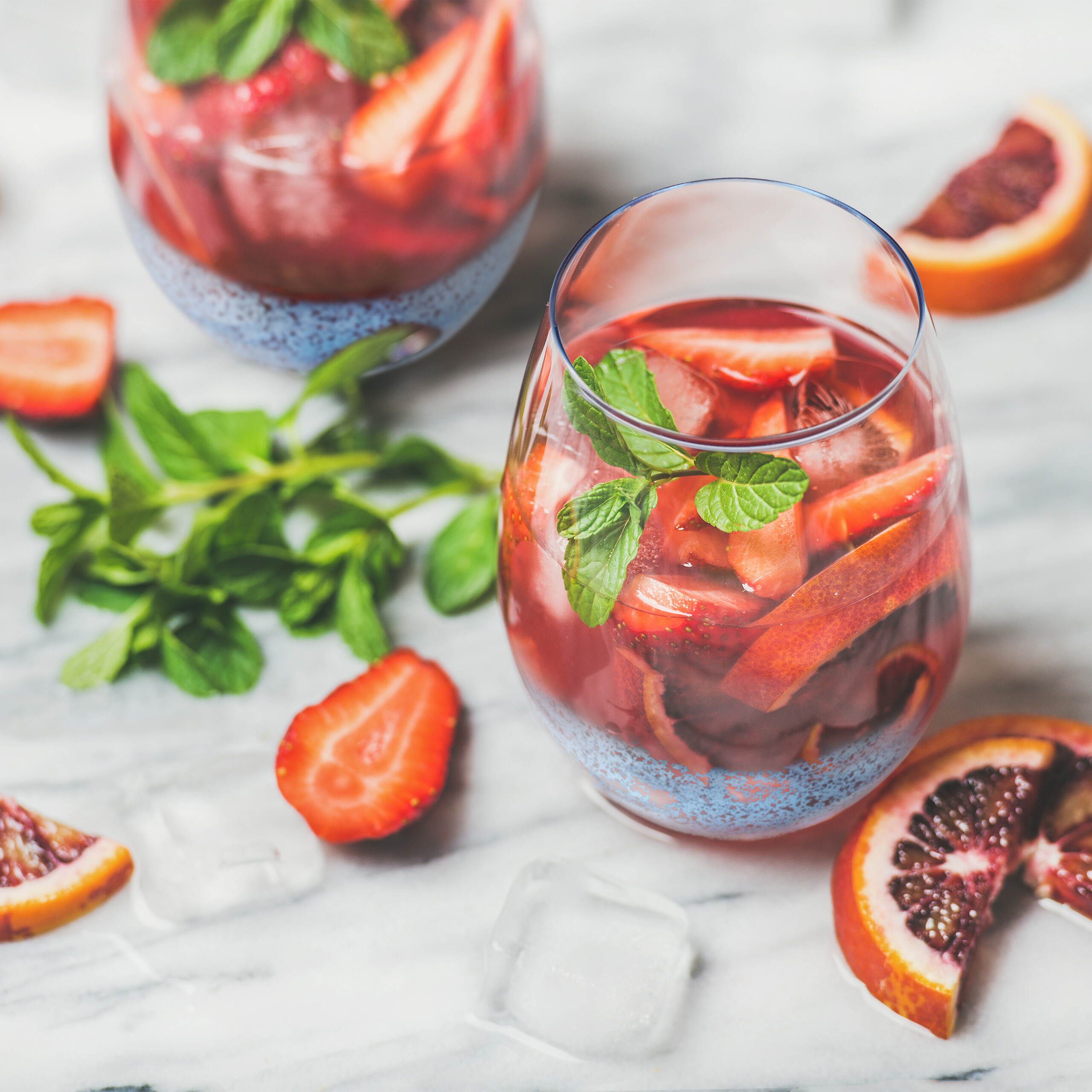 Zwei Gläser rote Fruchtbowle mit Erdbeeren, Minze, Orangen und Eis auf Marmor.