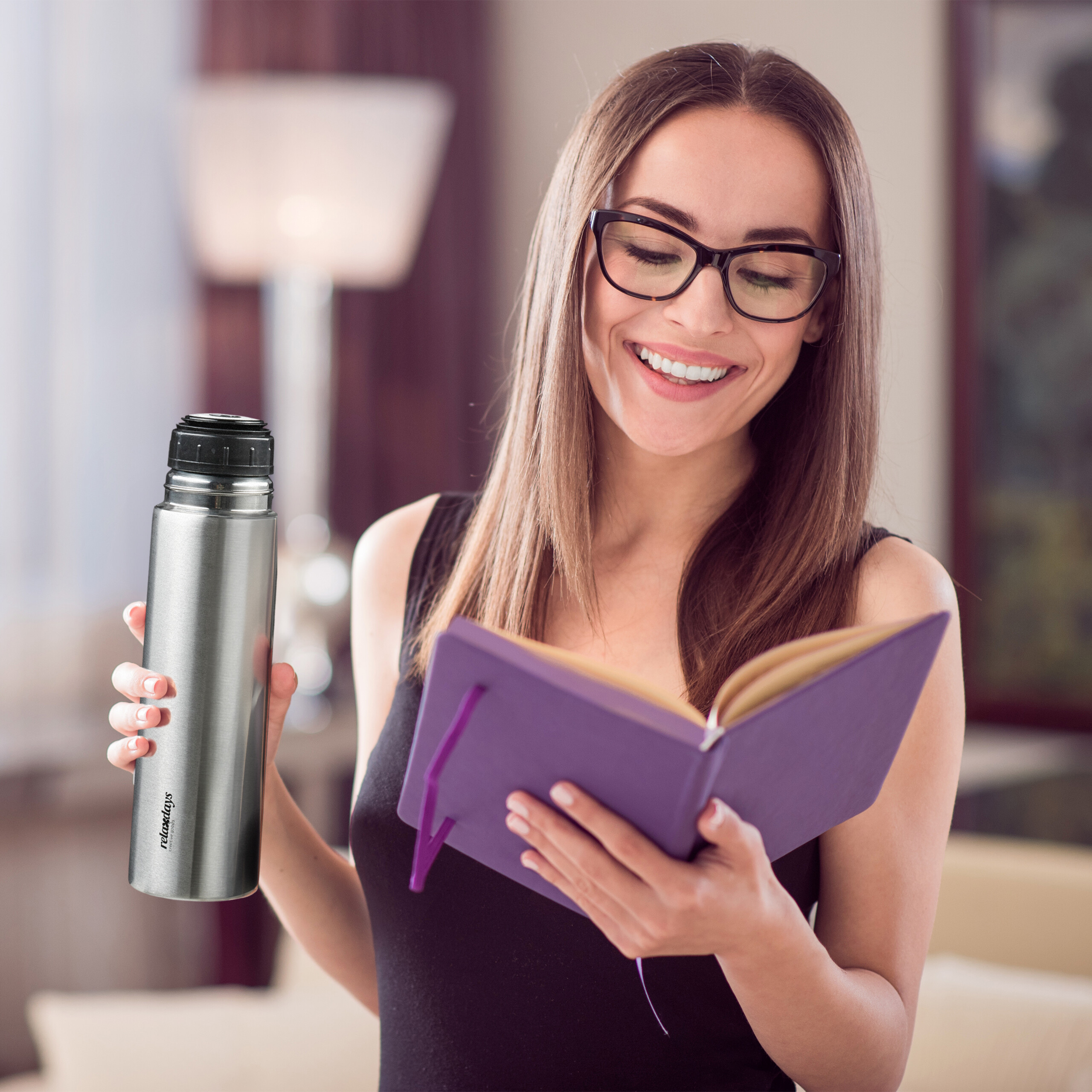 Eine lächelnde Frau in Brille liest ein Notizbuch und hält eine Thermoskanne.