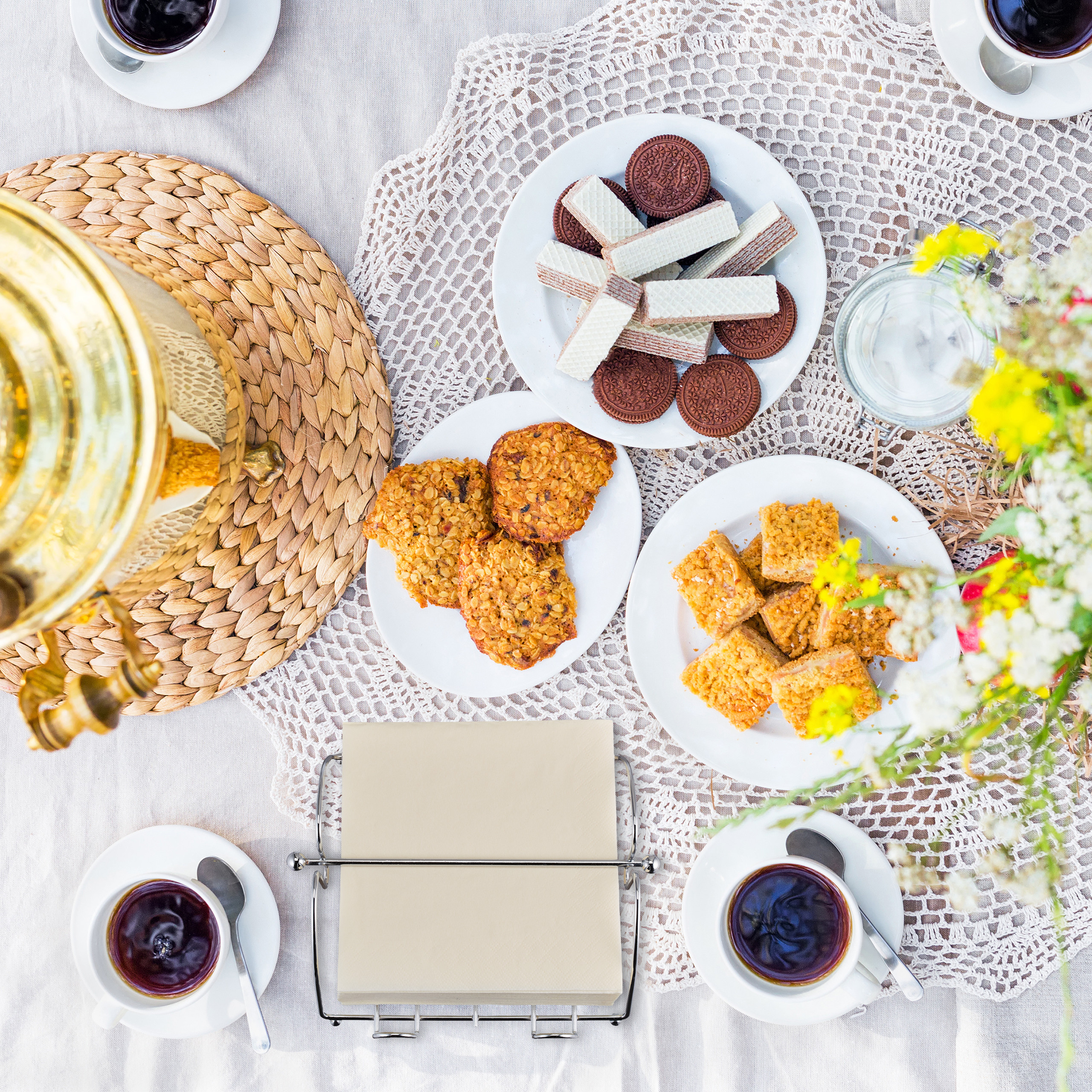 Gemütlicher Tisch mit Kaffeetassen, Gebäck, Keksen, einer Samowar und Blumen.