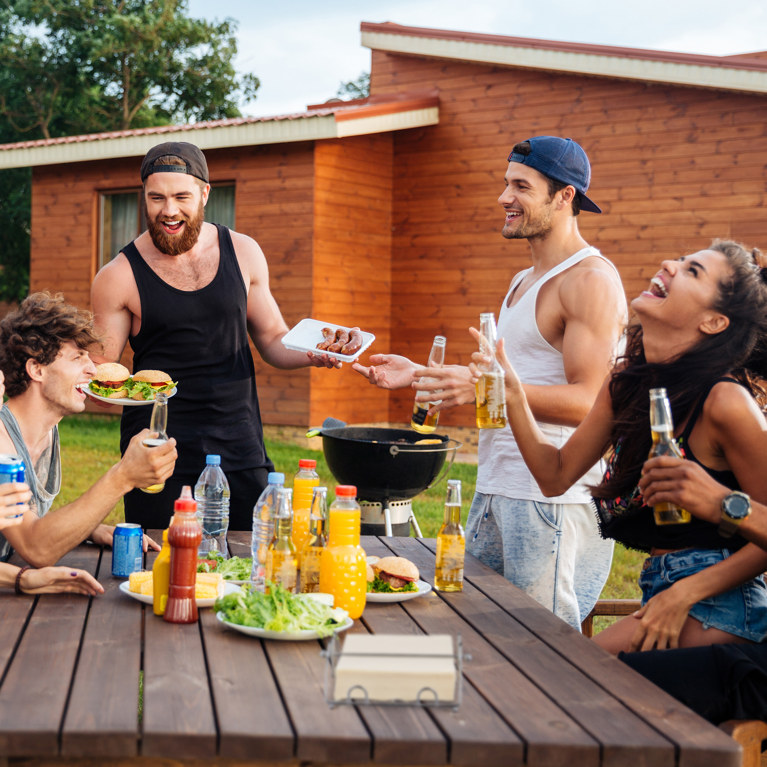 Freunde feiern eine Grillparty im Garten mit Burgern, Würstchen und Getränken.