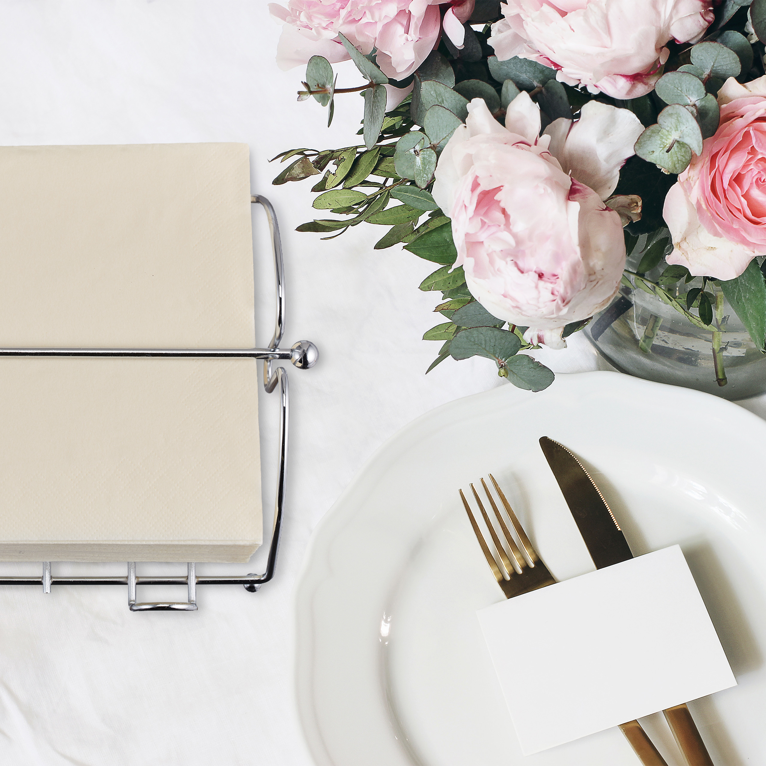 Ein eleganter Tisch mit weißem Teller, goldenem Besteck, leerer Namenskarte, Serviettenhalter und rosa Blumen.