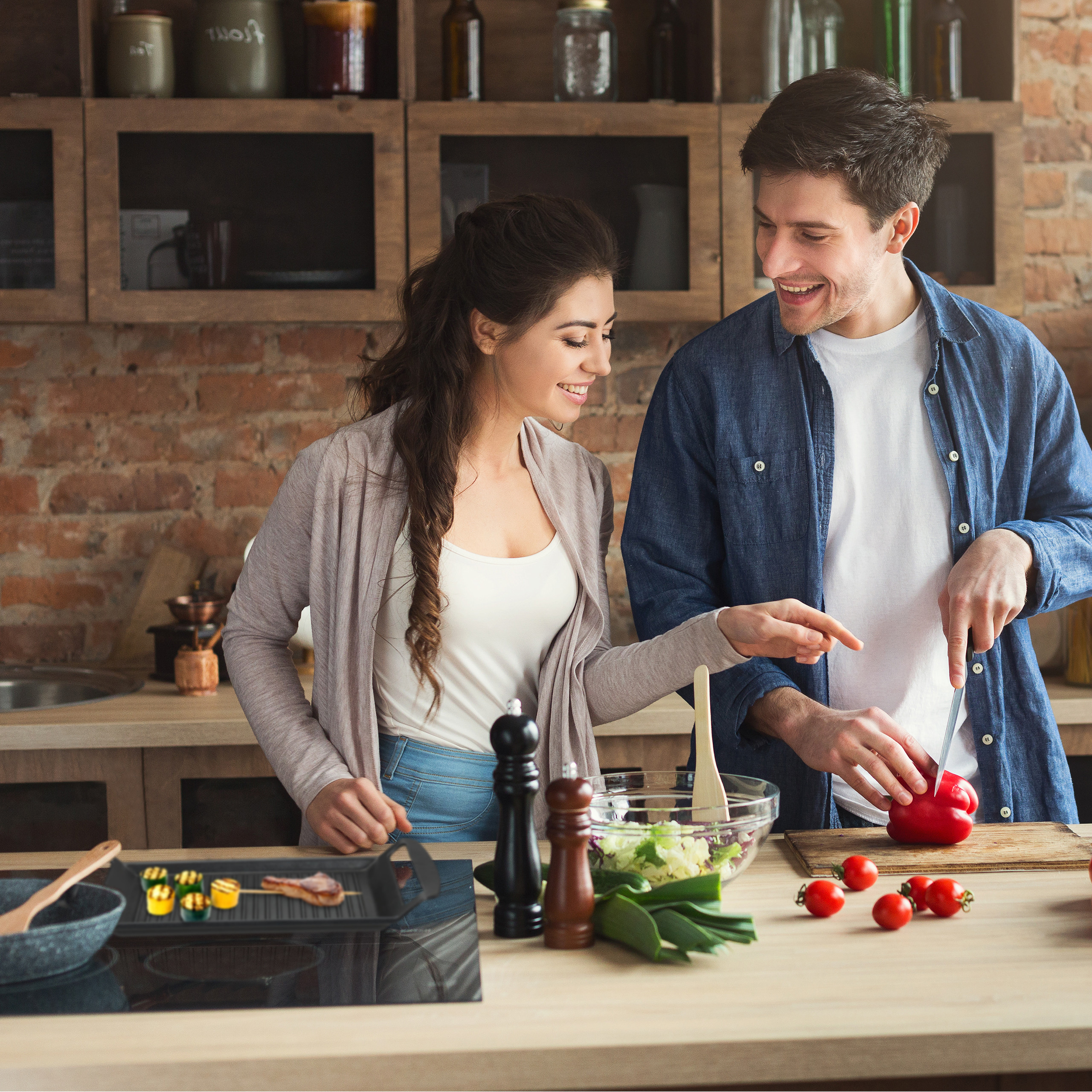 Ein junges Paar kocht zusammen in einer Küche, schneidet roten Paprika und bereitet einen Salat zu.