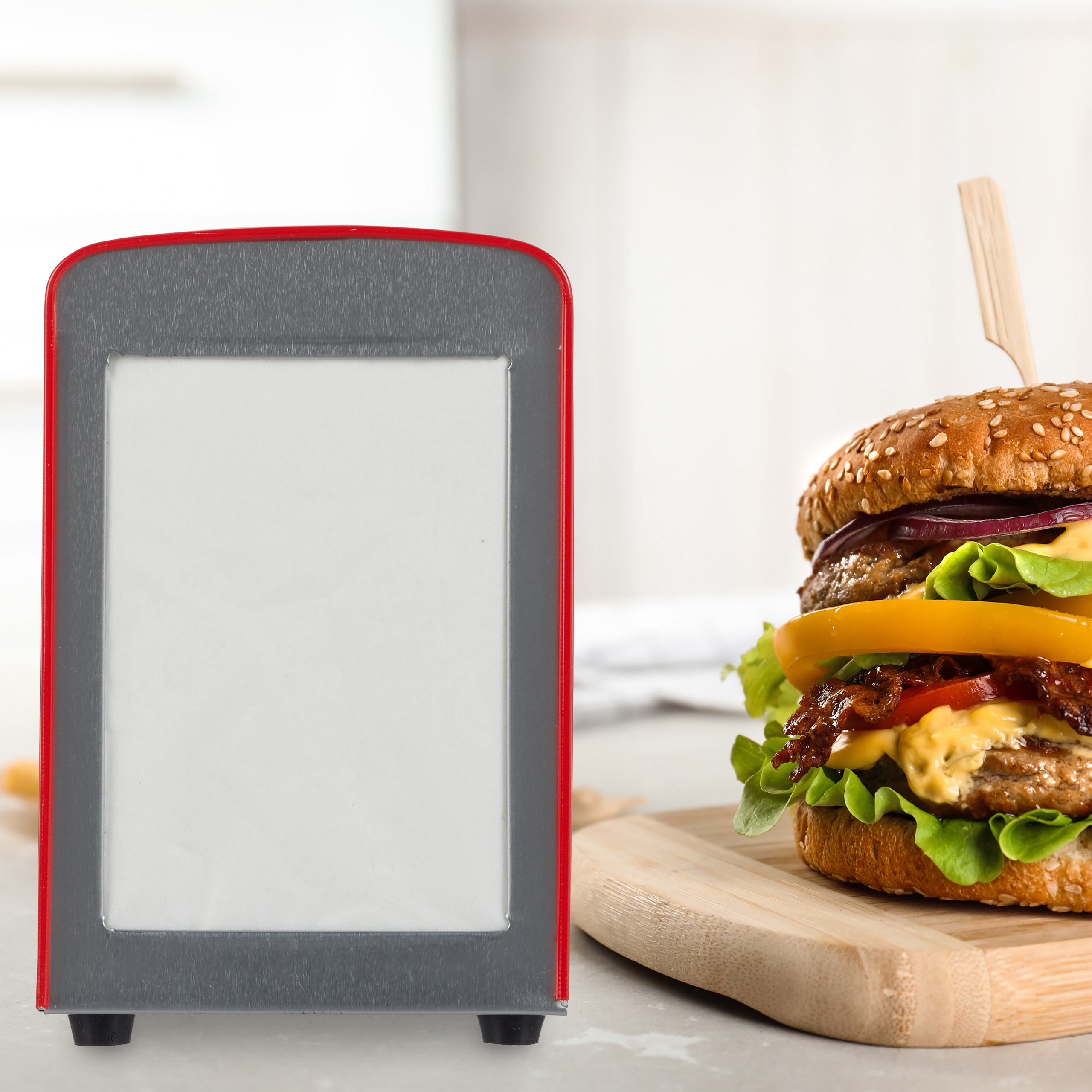 Ein roter Serviettenhalter steht neben einem großen Burger auf einem Holzbrett vor weißem Hintergrund.