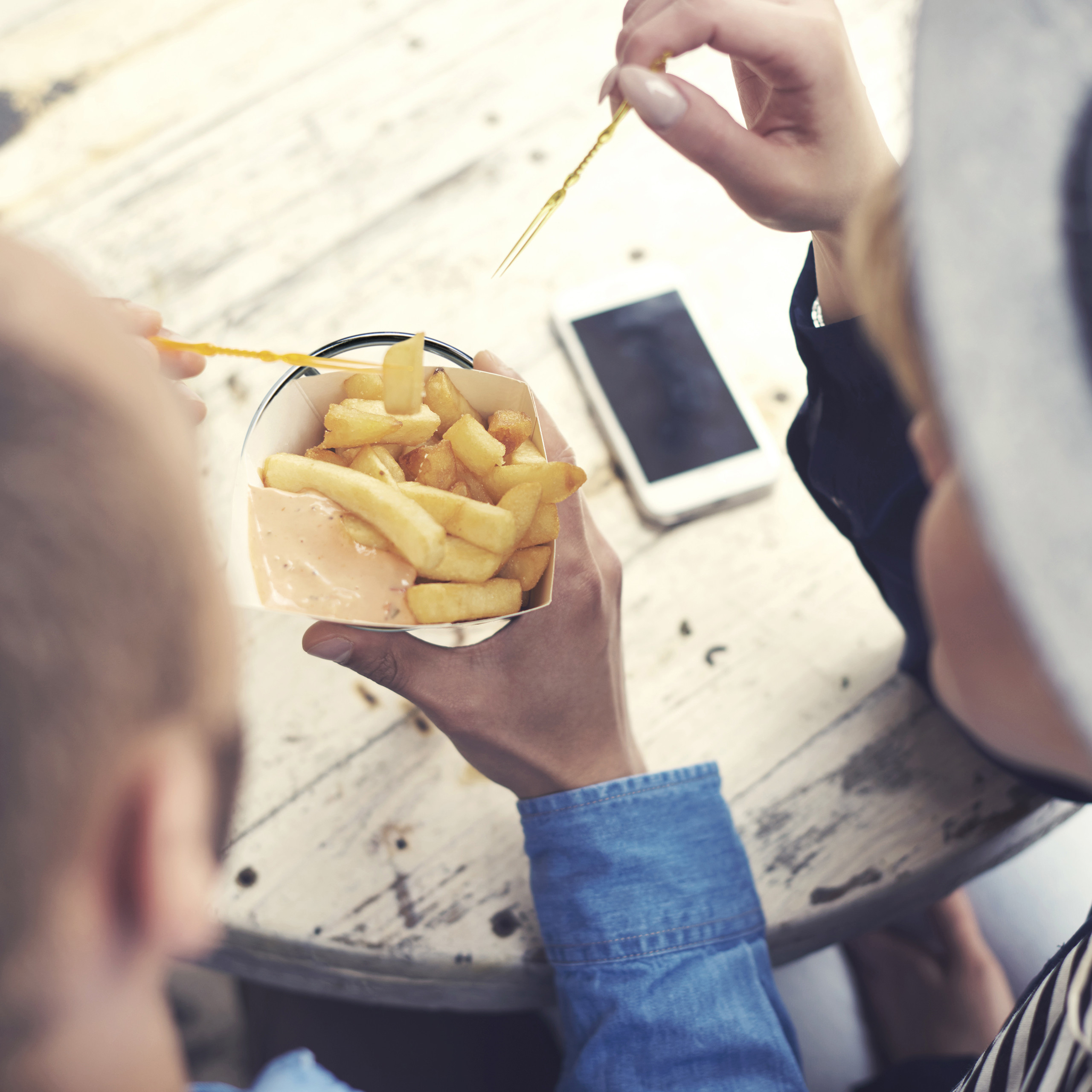 Zwei Personen essen Pommes mit Saucen auf einem Holztisch.