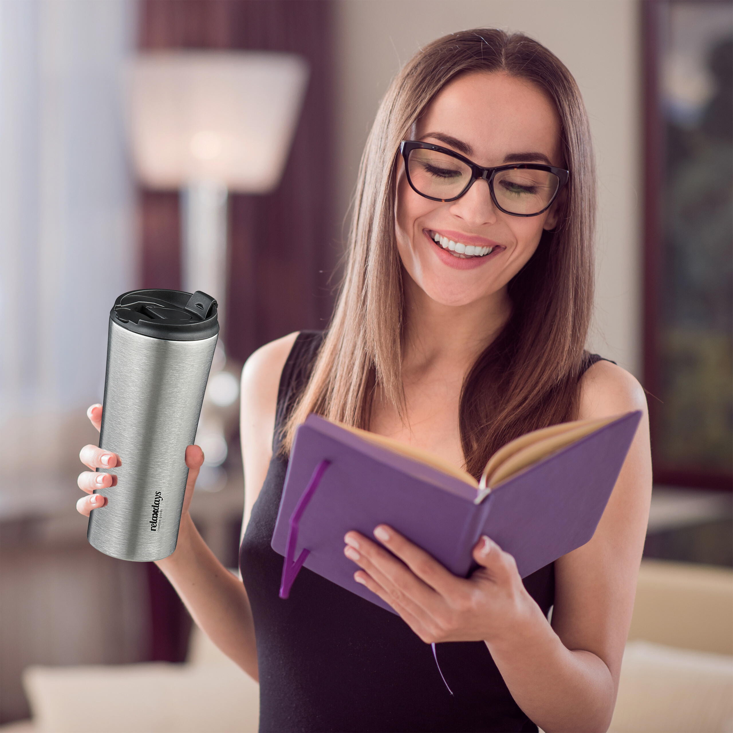 Eine lächelnde Frau in Brille liest ein Notizbuch und hält einen silbernen Thermobecher.