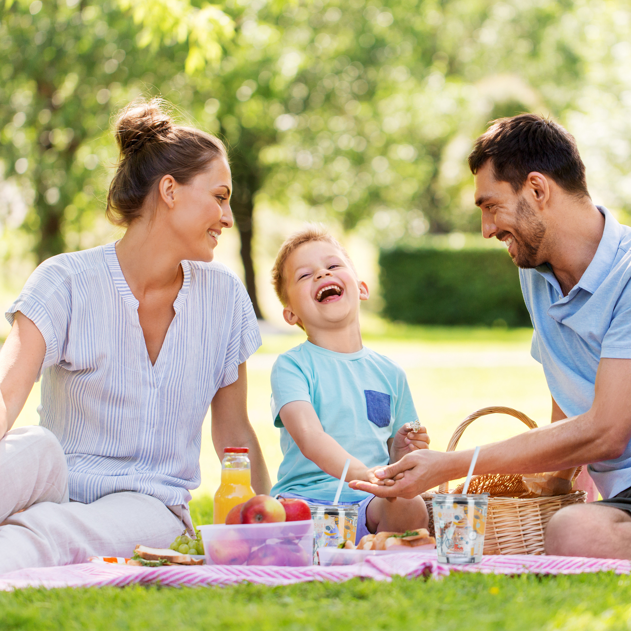 Eine glückliche Familie genießt ein Picknick im Park mit Obst, Getränken und einem lachenden Kind.
