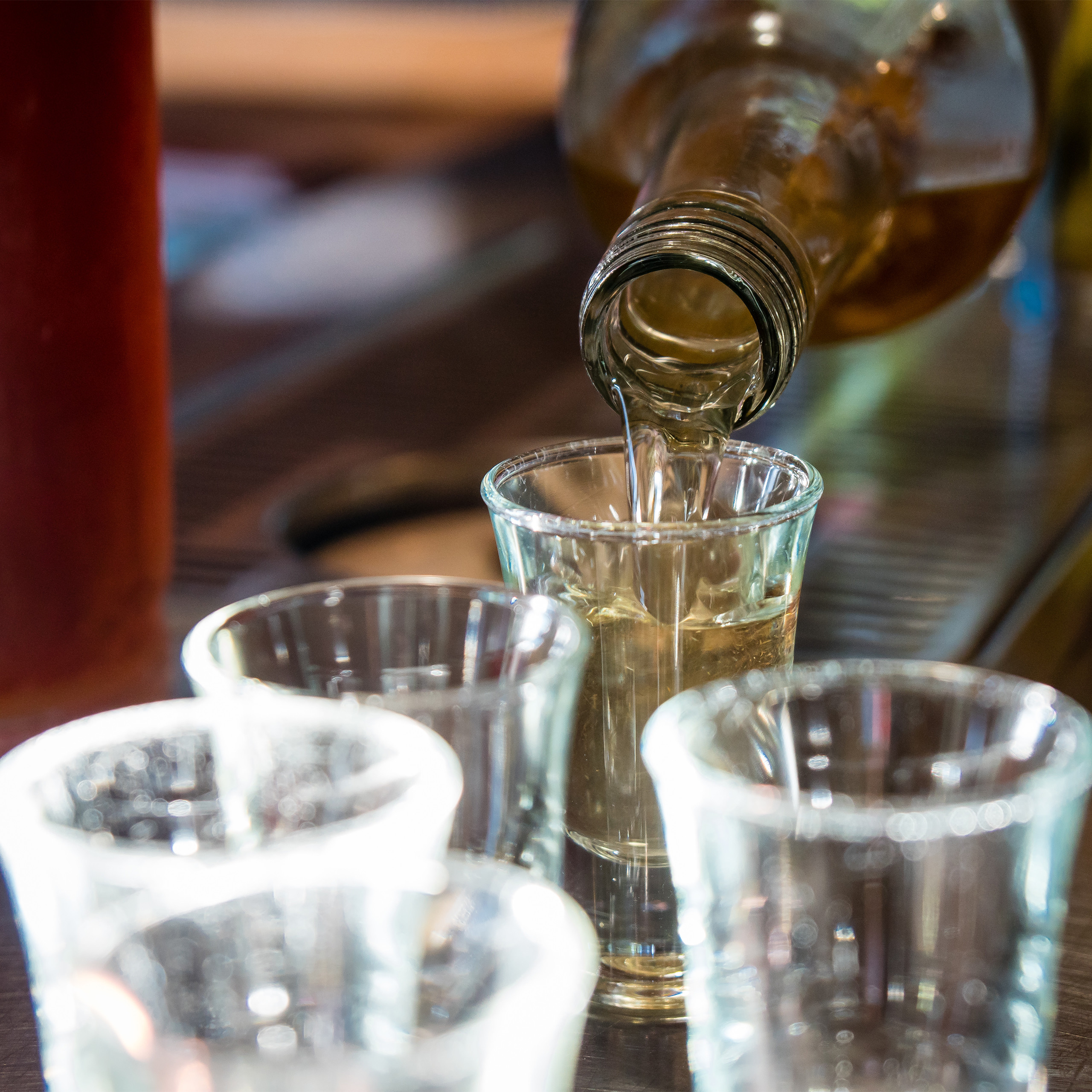 Eine Flasche gießt Alkohol in ein kleines Schnapsglas, während andere Gläser auf der Bar stehen.