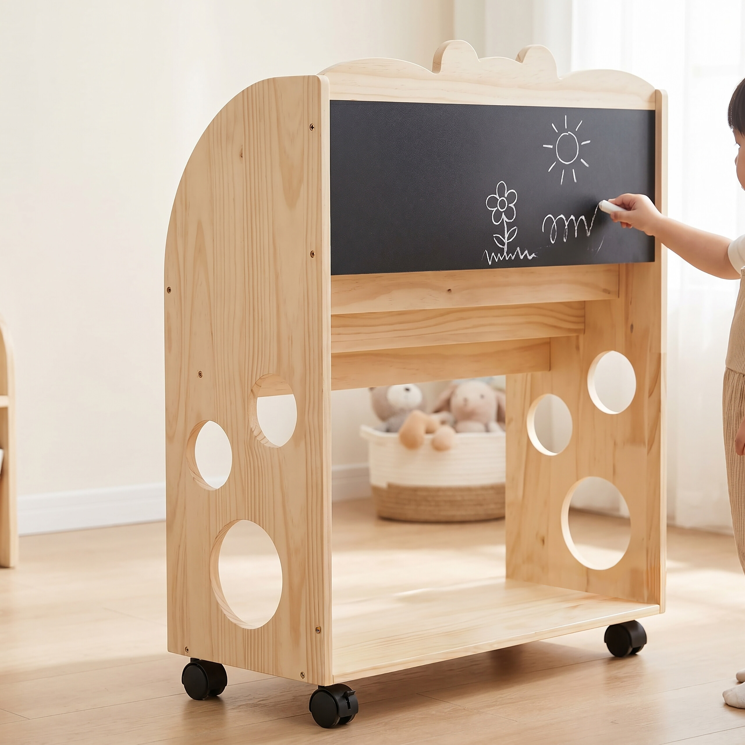 Ein Kind zeichnet mit Kreide auf einen Holzwagen mit Tafel, kreisrunden Aussparungen und einem Aufbewahrungskorb.