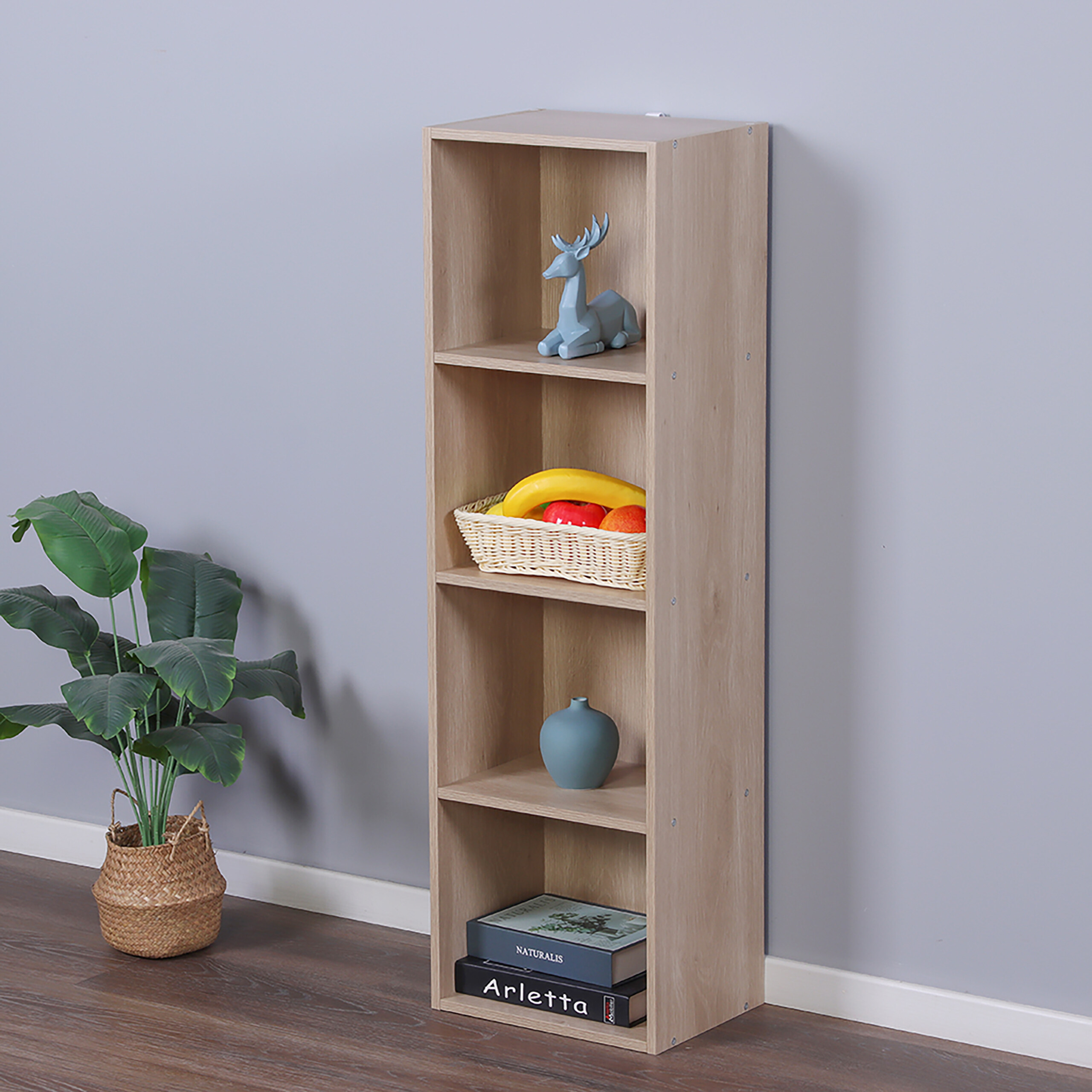 Ein helles vierteiliges Holzregal an grauer Wand mit Hirschfigur, Obstkorb, Vase und Büchern.