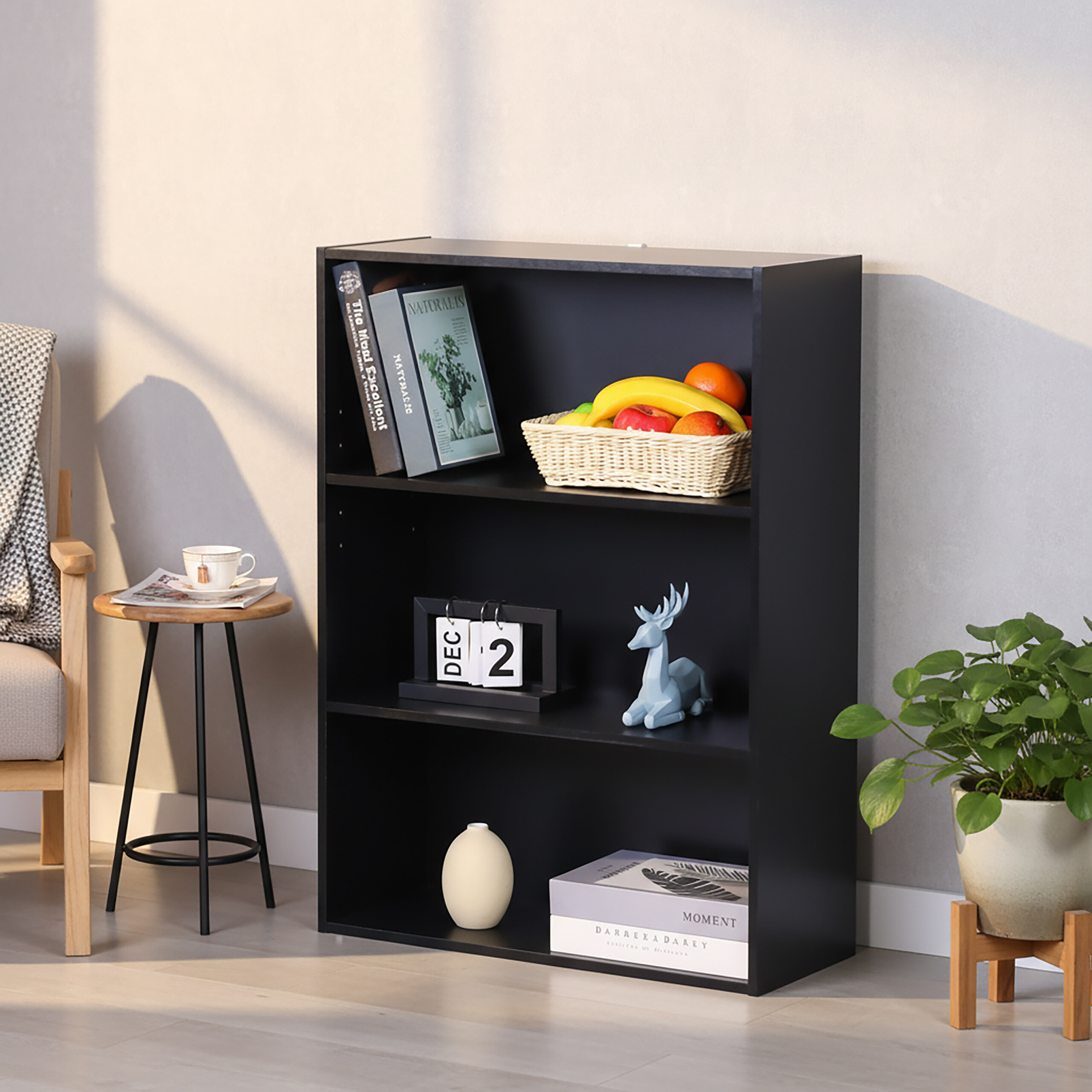 Ein schwarzes dreistöckiges Bücherregal hält Bücher, Obstkorb, Kalender, Hirschfigur und Vase.