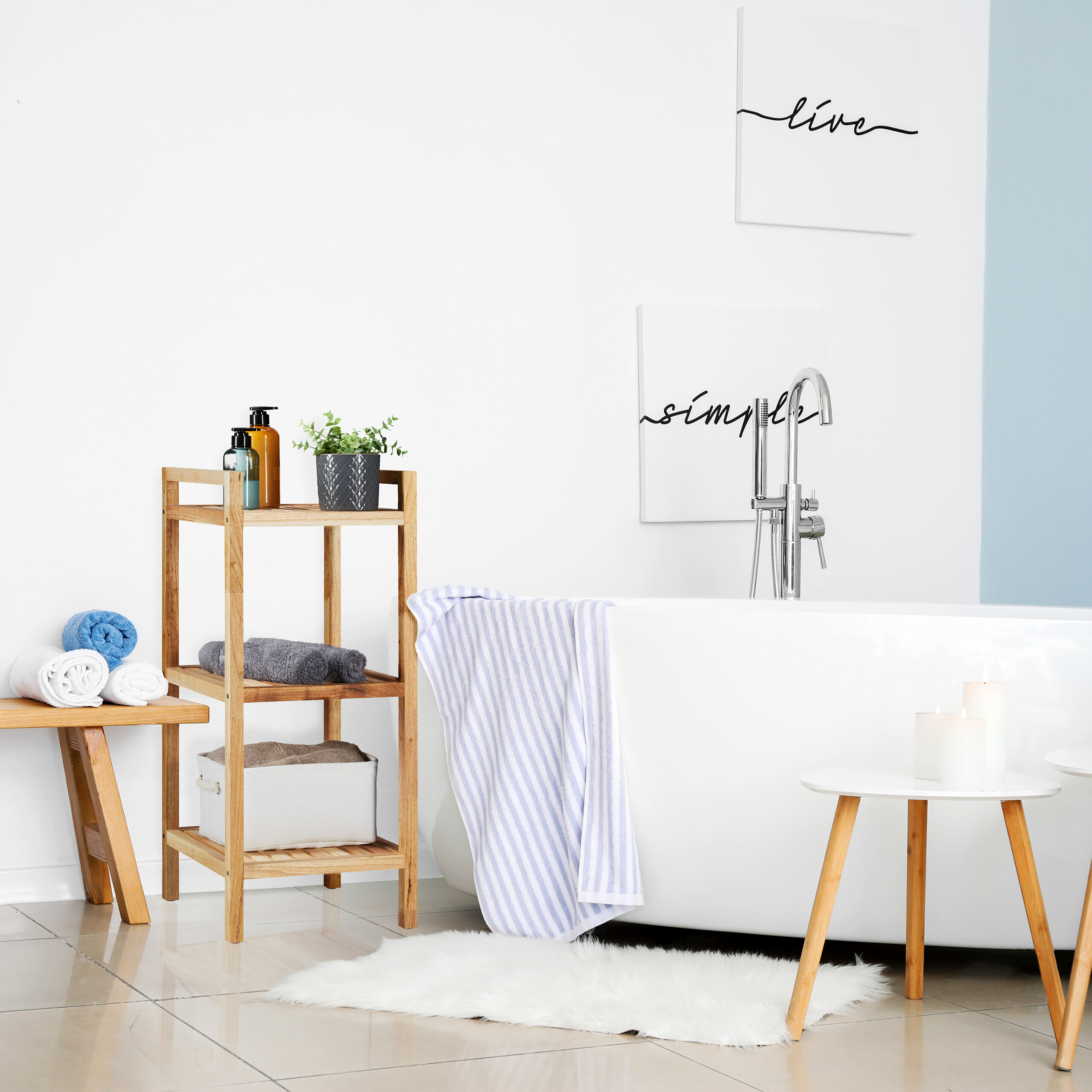 Moderne weiße Badewanne mit Holzdurchgangsregal, Handtüchern und Wandkunst in einem hellen Raum.