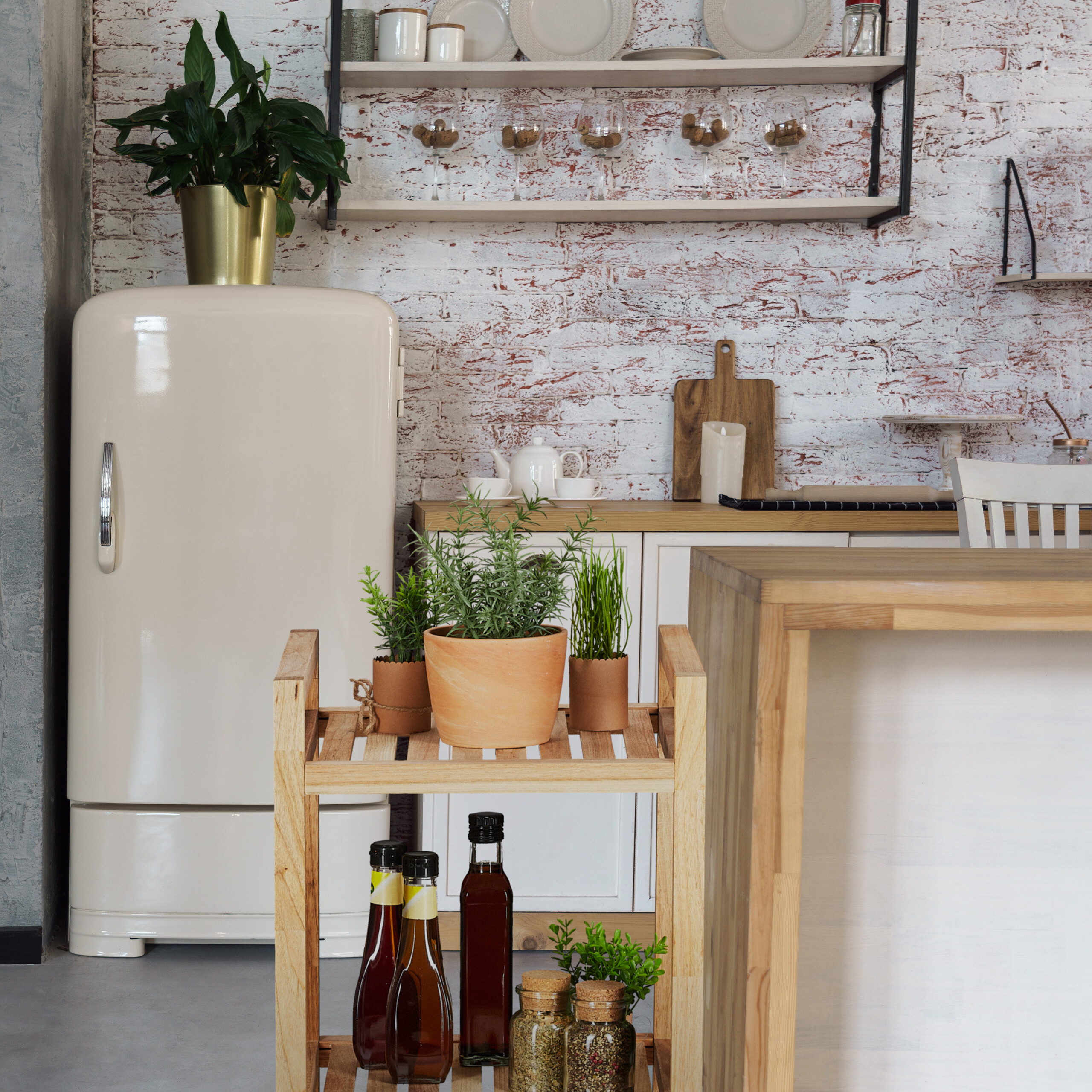 Moderne Küche mit weißer Backsteinwand, cremefarbenem Retro-Kühlschrank, Holzregalen und Pflanzen auf einem Wagen.
