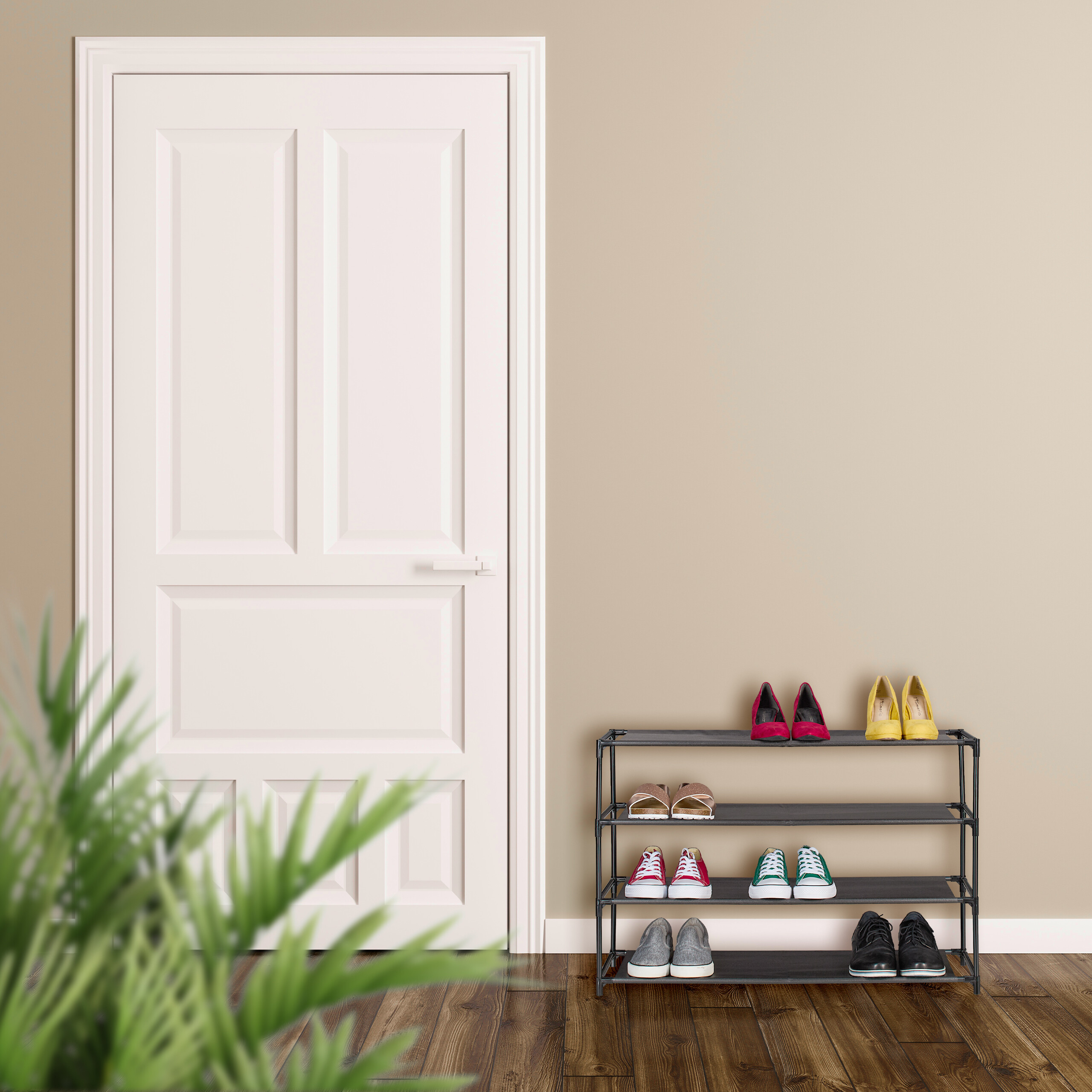 Ein Schuhregal mit bunten Schuhen steht neben einer weißen Tür und einer beigen Wand, im Vordergrund ist eine Pflanze.