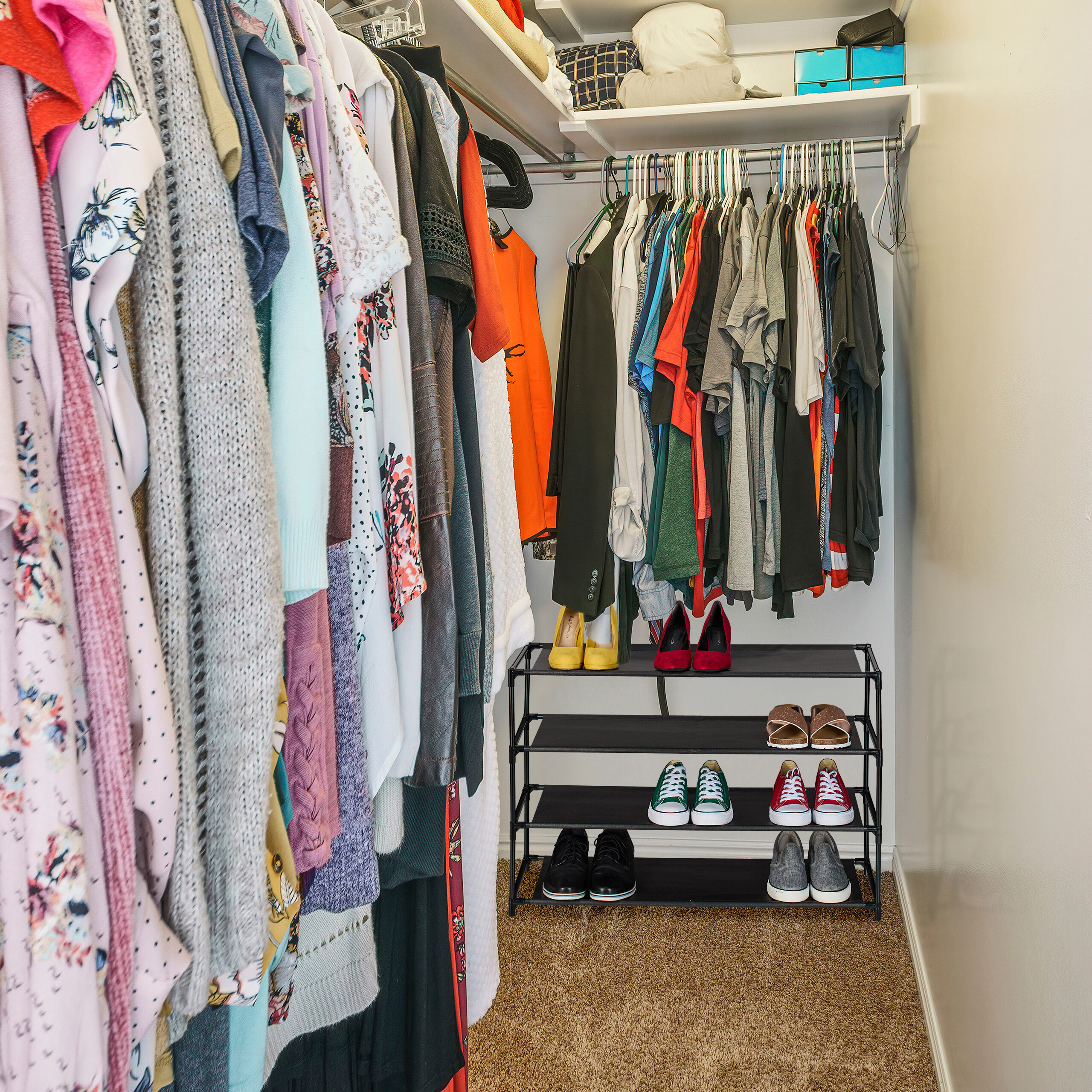 Ein begehbarer Kleiderschrank voll mit britbunter Kleidung, Hängestangen und einem kleinen schwarzen Schuhregal.