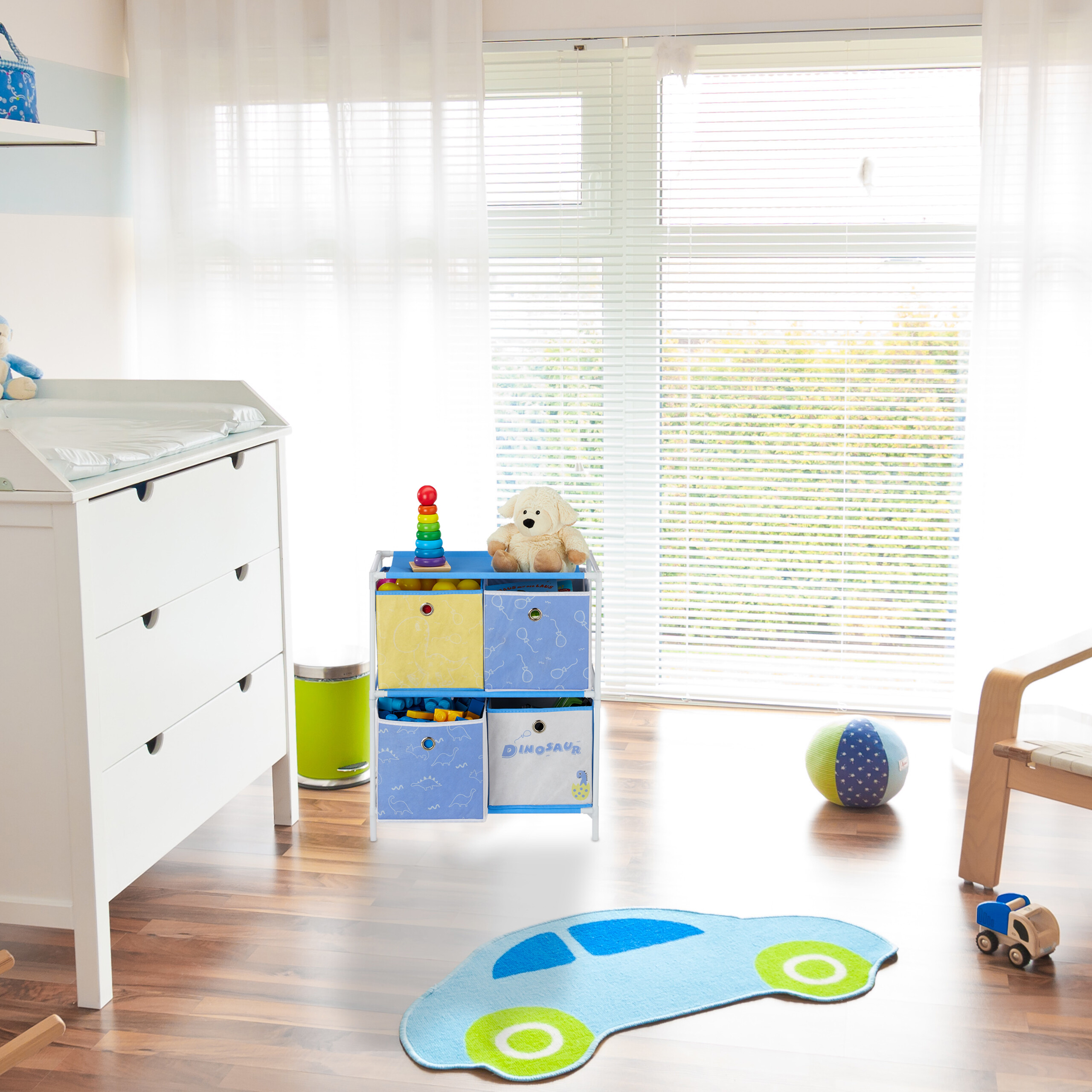 Ein helles Kinderzimmer mit weißer Kommode, blauem Spielzeugregal, Auto-Teppich und großen Fenstern mit Jalousien.