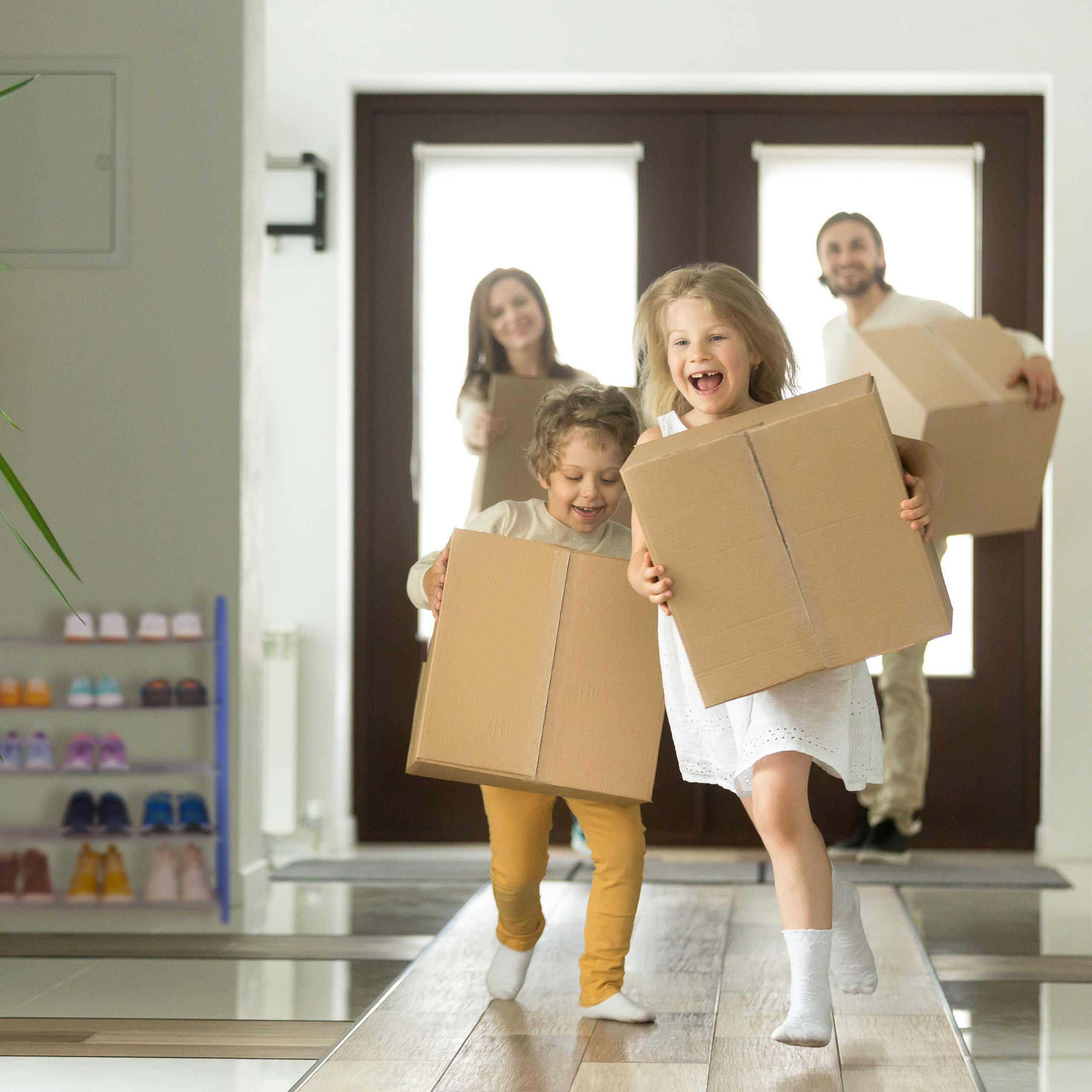 Glückliche Kinder und Eltern tragen Umzugskartons in einen neuen Flur.