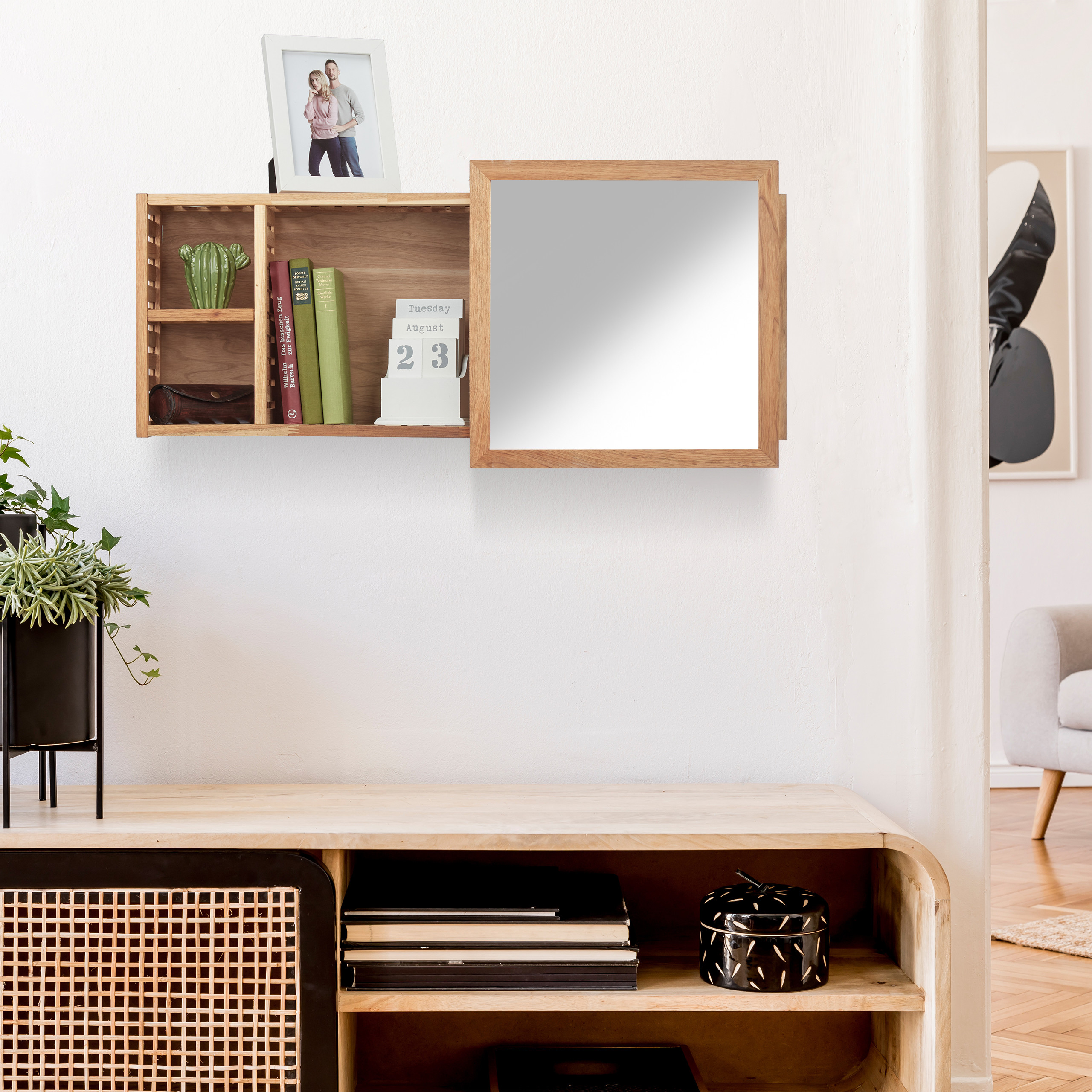 Wandregal mit Spiegel, Büchern und Dekoration über einem Holzschrank in einem weißen Zimmer.