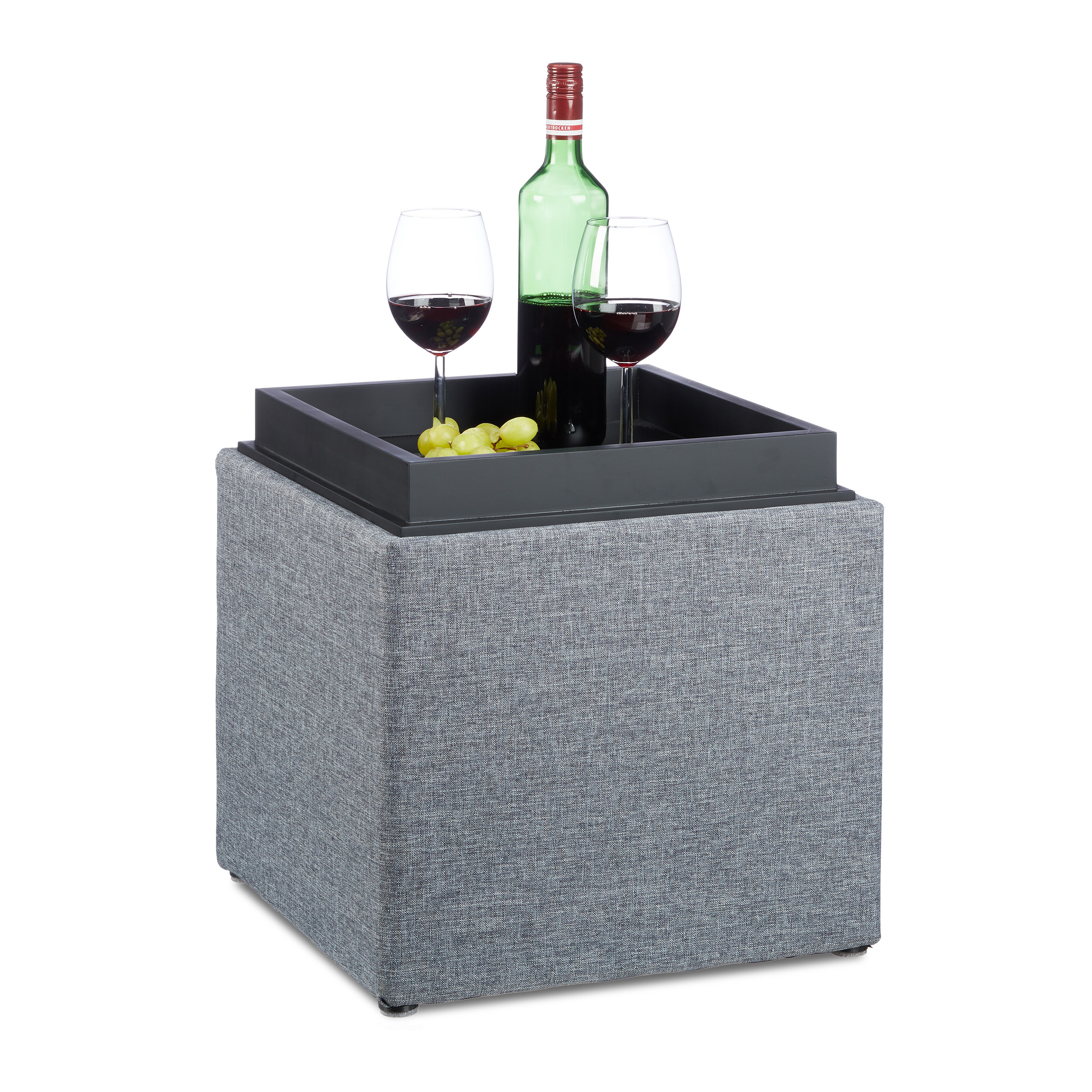 Ein grauer Polsterhocker mit schwarzem Tablett, Weinflasche, zwei Gläsern und grünen Trauben darauf.