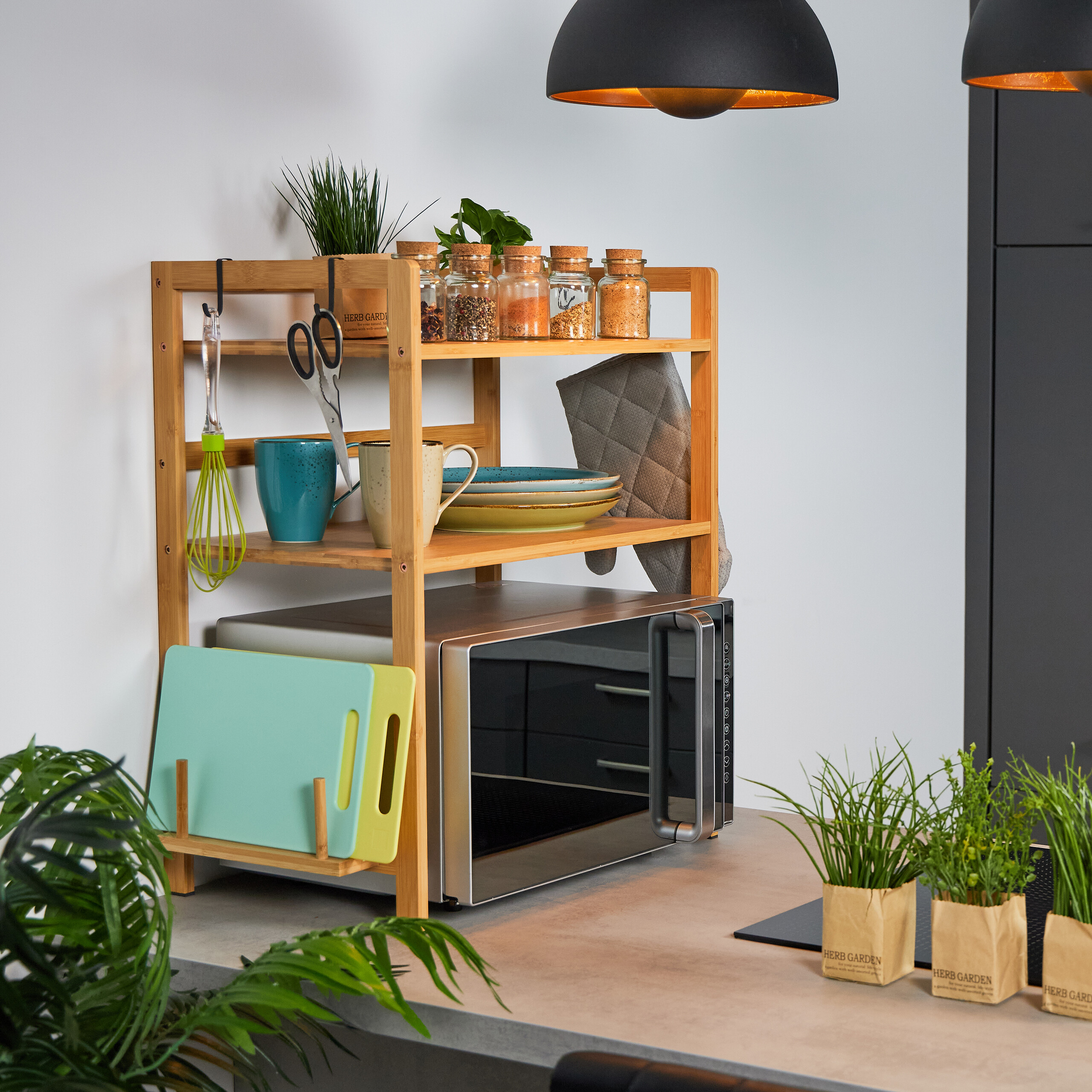 Holzregal auf Mikrowelle mit Gewürzen, Tassen, Tellern, Scheren und Pflanzen in moderner Küche.