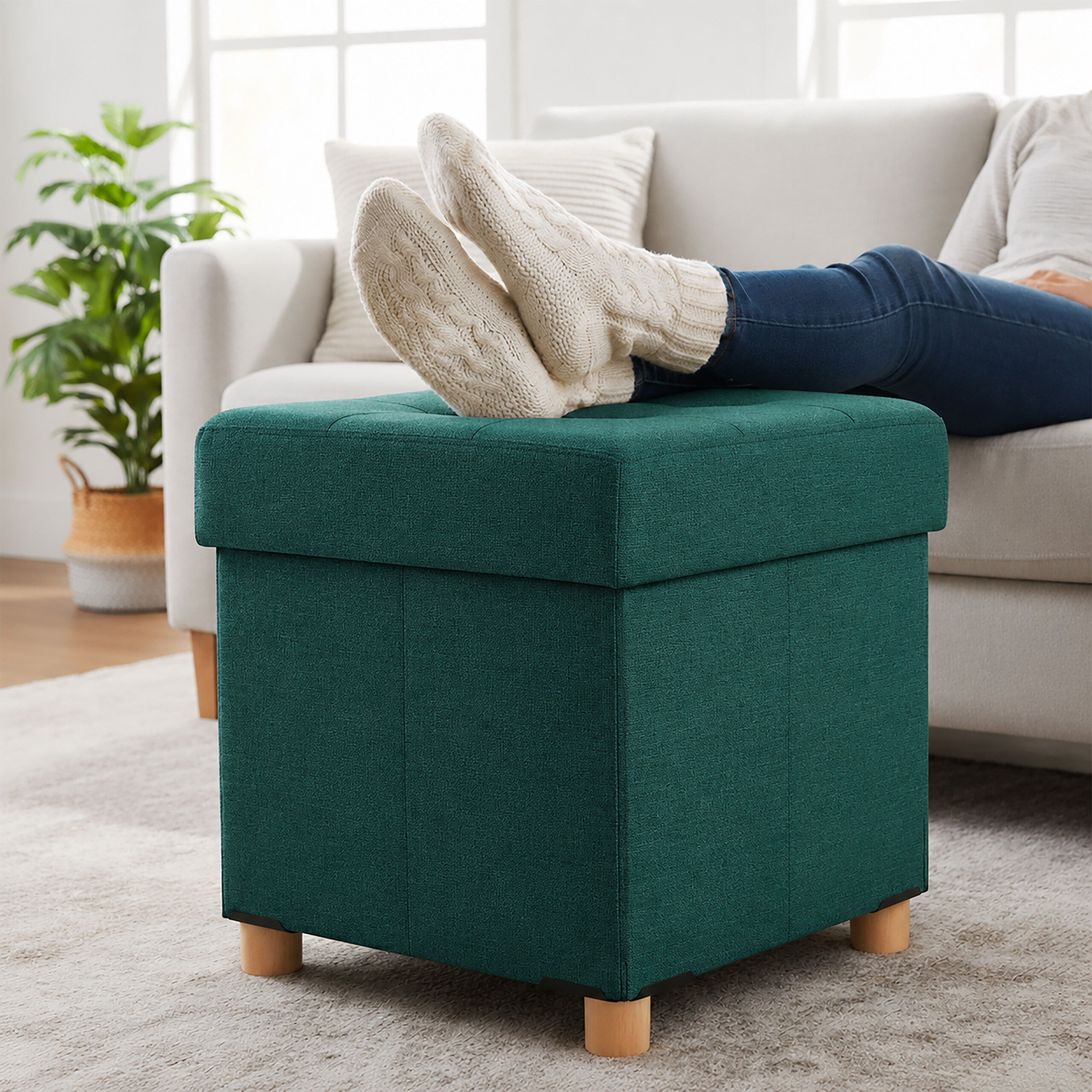 Person liegt auf einer Couch mit den Füßen in cremefarbenen Stricksocken auf einem dunkelgrünen Hocker.