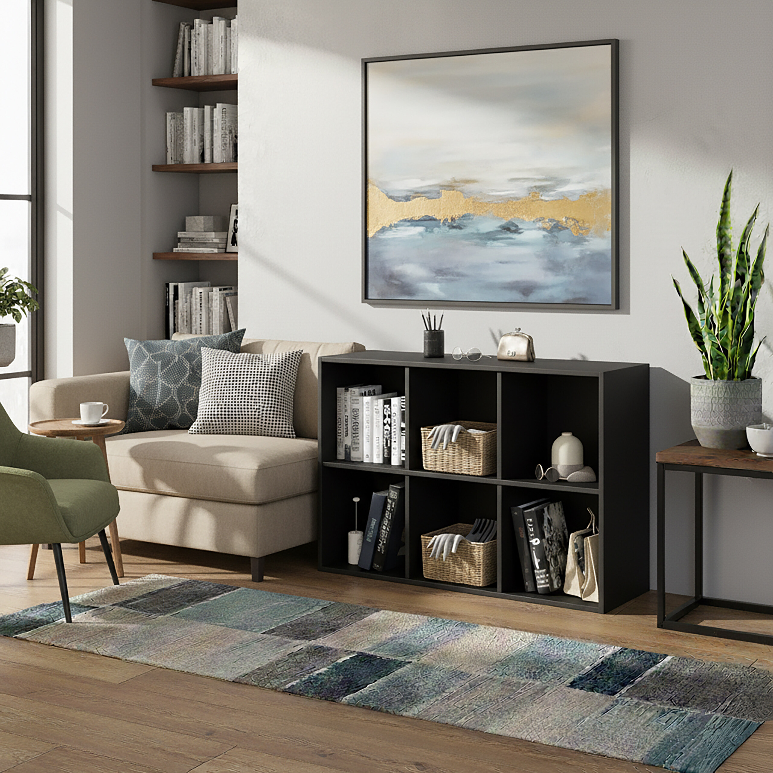 Ein Wohnzimmer mit einem beigen Sofa, schwarzem Regal mit Büchern, Wandkunst und gemustertem Teppich.
