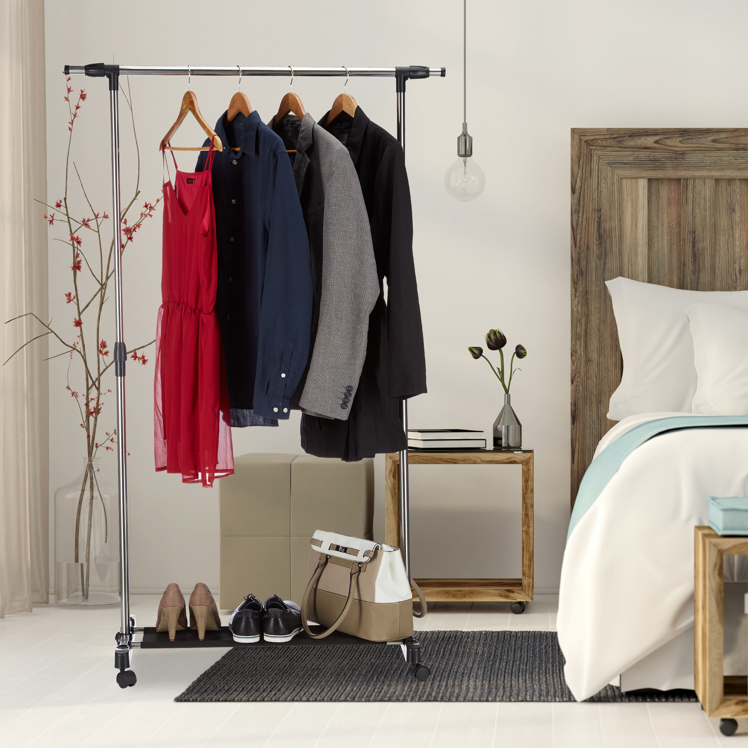 Ein Kleiderständer aus Metall mit Kleidern, Hemden und Jacken, Schuhen und einer Handtasche im Schlafzimmer.