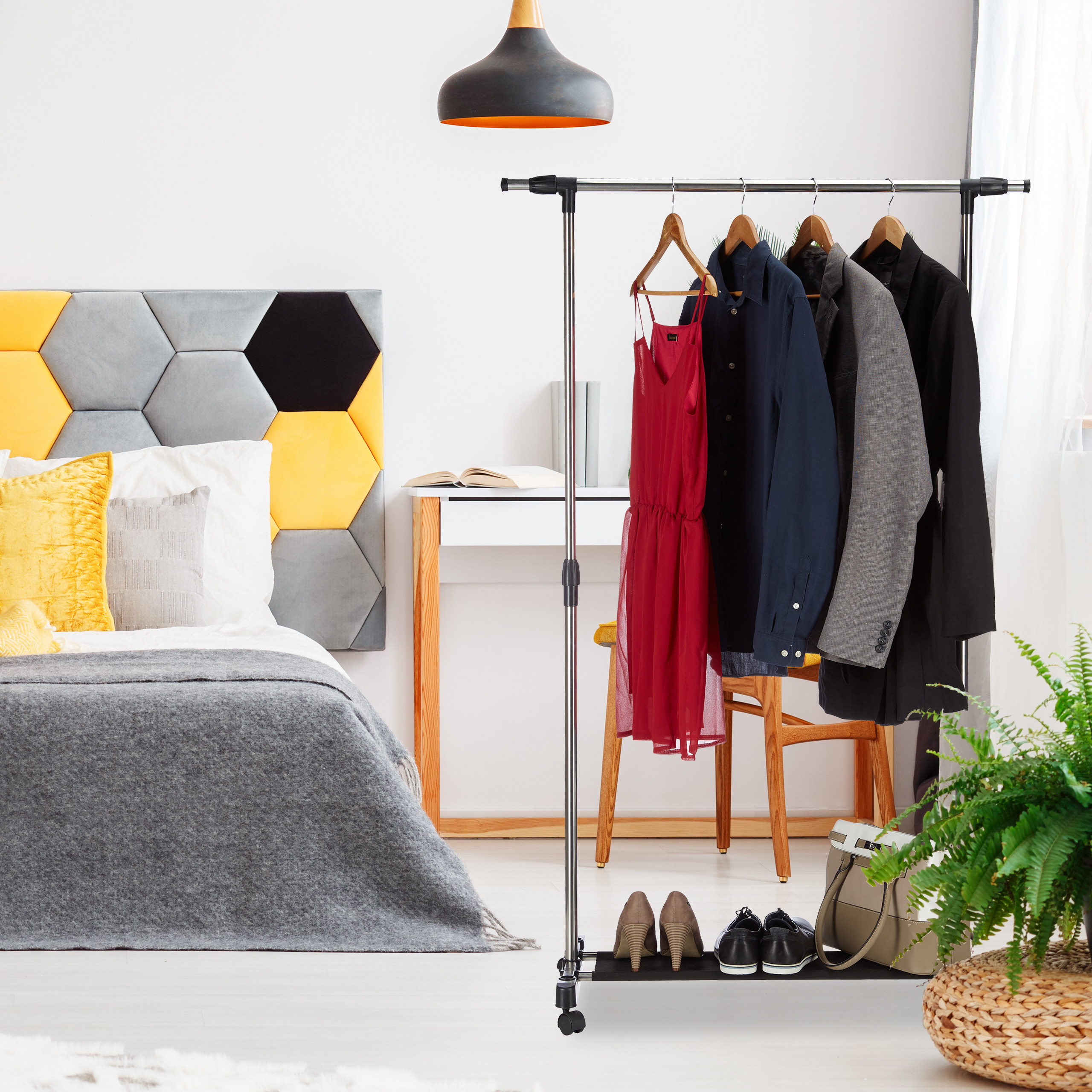 Kleiderständer mit Kleidung, Schuhen und Tasche im Schlafzimmer neben dem Bett mit gelb-grauem Kopfteil.