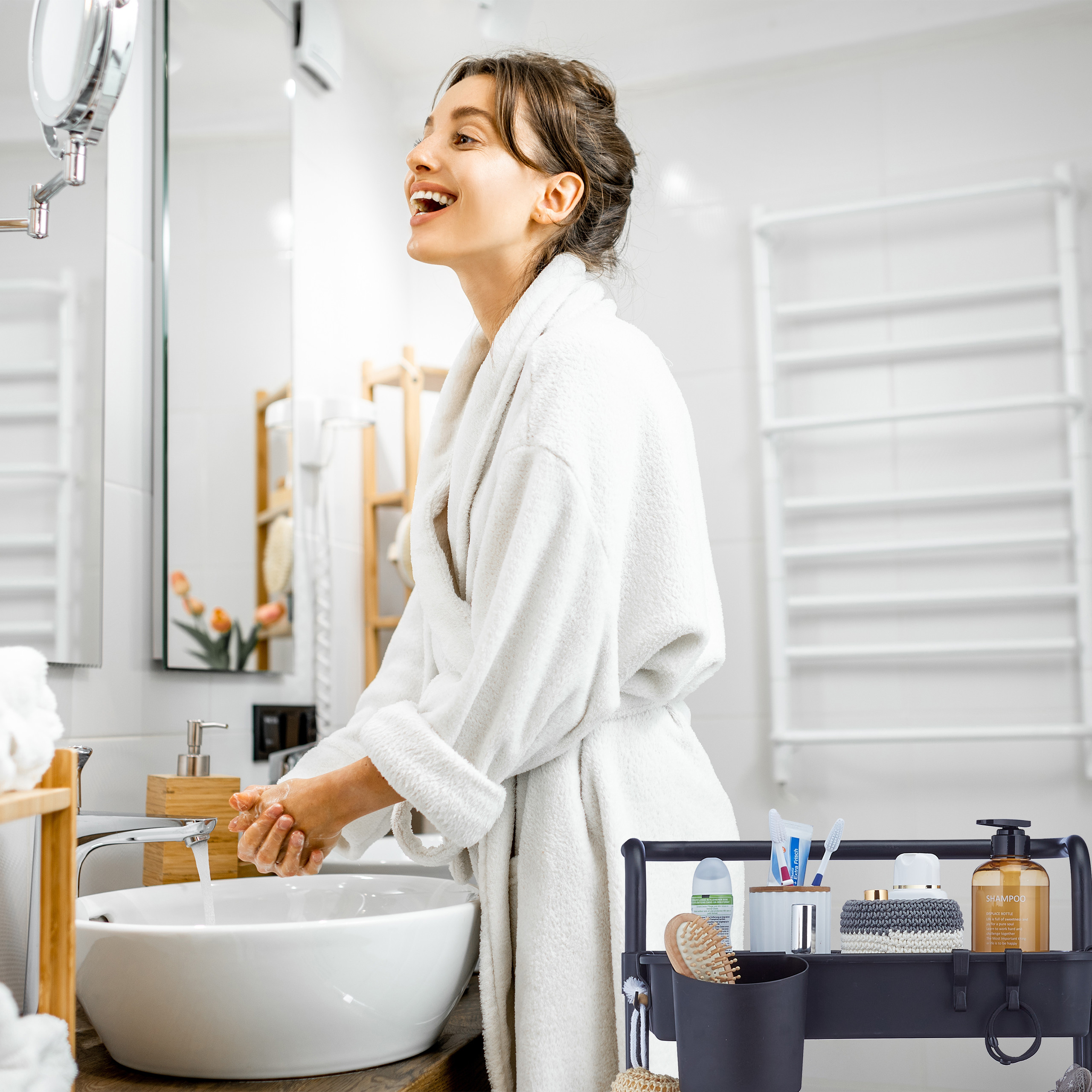 Eine lächelnde Frau im Bademantel wäscht sich im modernen Badezimmer die Hände am Waschbecken.