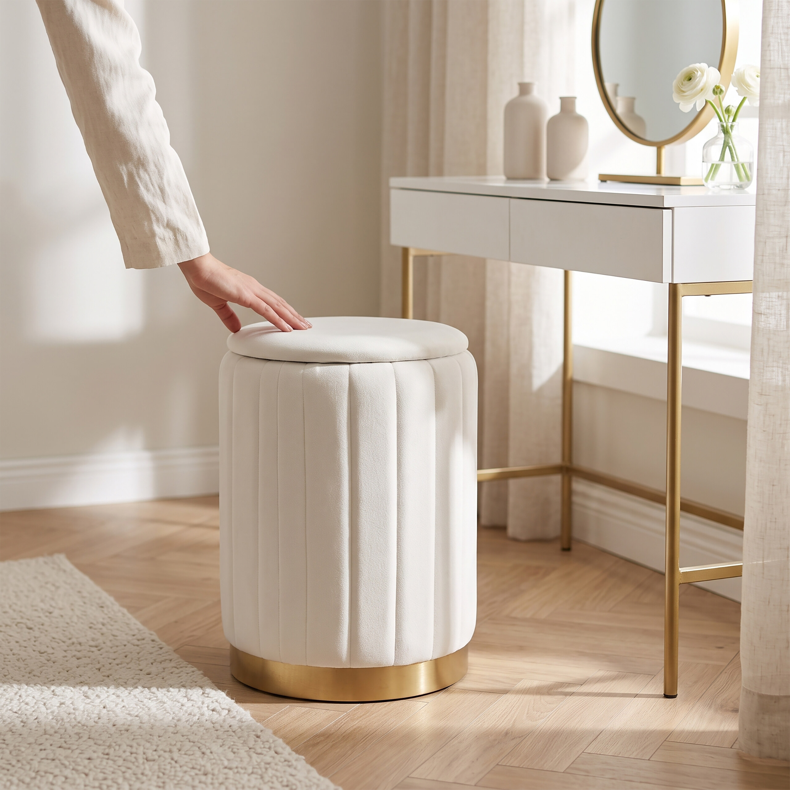 Eine Hand berührt einen runden, weißen Hocker mit goldenem Fuß vor einem Schminktisch.