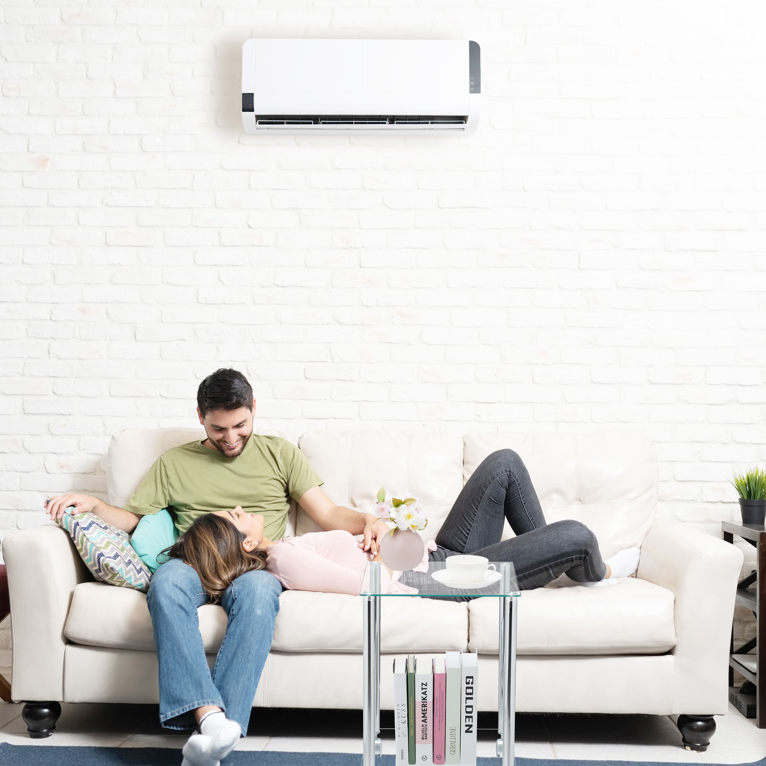 Ein Paar ruht auf einer weißen Couch unter einer Klimaanlage in einem Raum mit weißen Backsteinwänden.