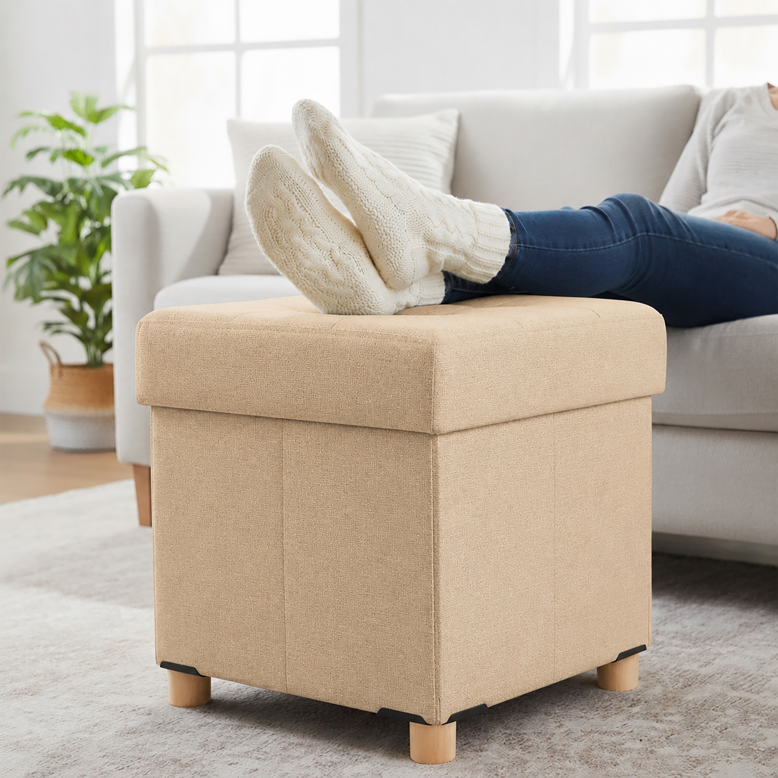 Eine Person sitzt auf einer Couch und legt die Füße in weißen Strickstrümpfen auf einen beigen Hocker.