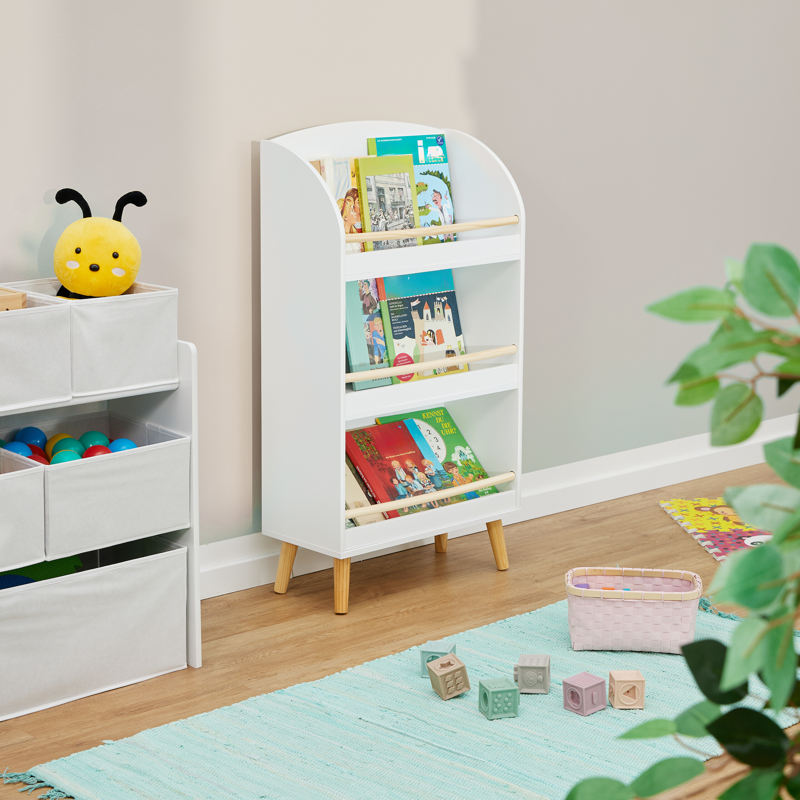 Kinderzimmer mit weißem Bücherregal, Spielzeugkisten, Plüschbiene und Spielzeug auf einem blauen Teppich.