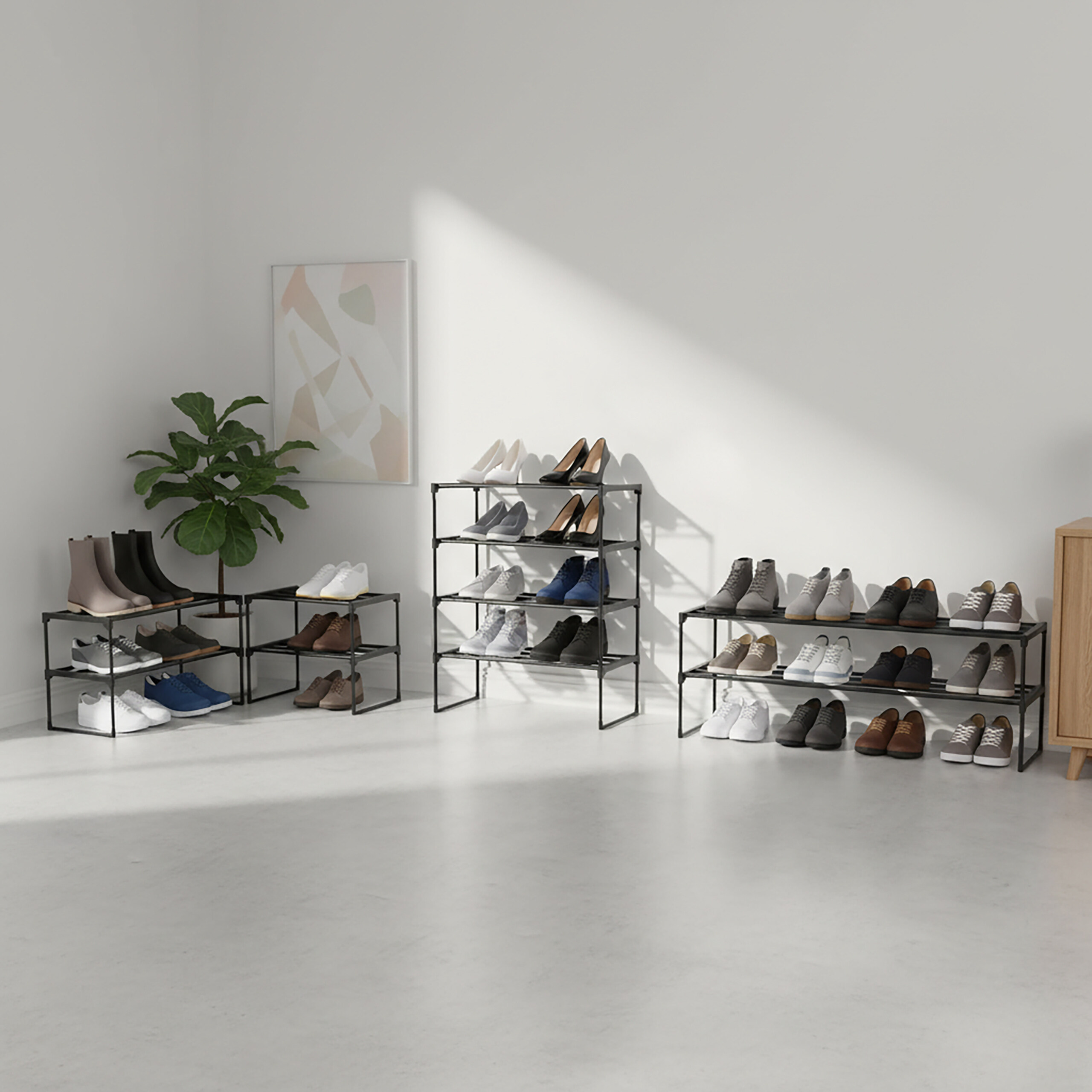 Ein heller Raum zeigt drei schwarze Metall-Schuhregale mit verschiedenen Schuhen, eine Topfpflanze und Wandkunst.