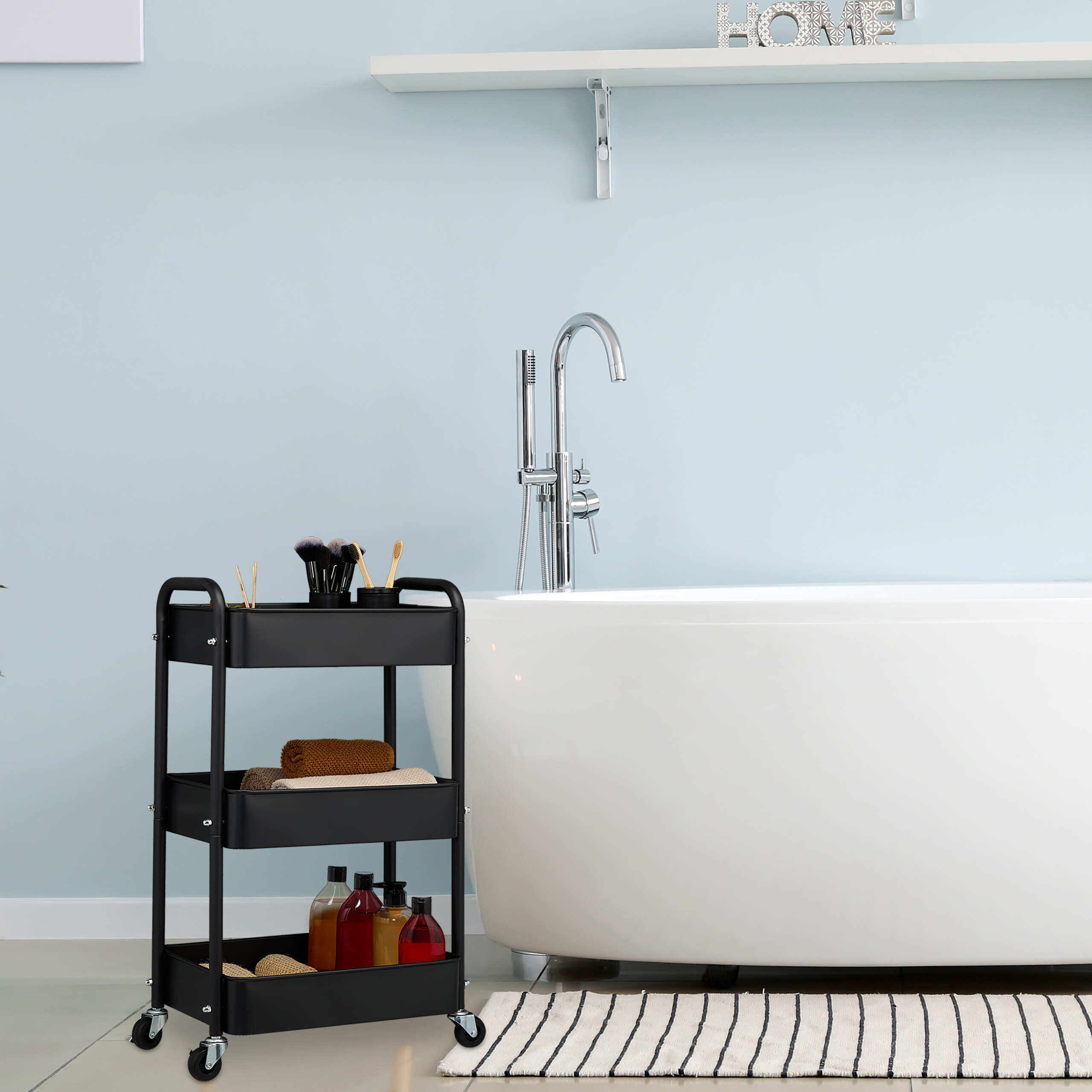 Ein schwarzer dreistöckiger Servierwagen steht neben einer weißen Badewanne in einem hellblauen Badezimmer.