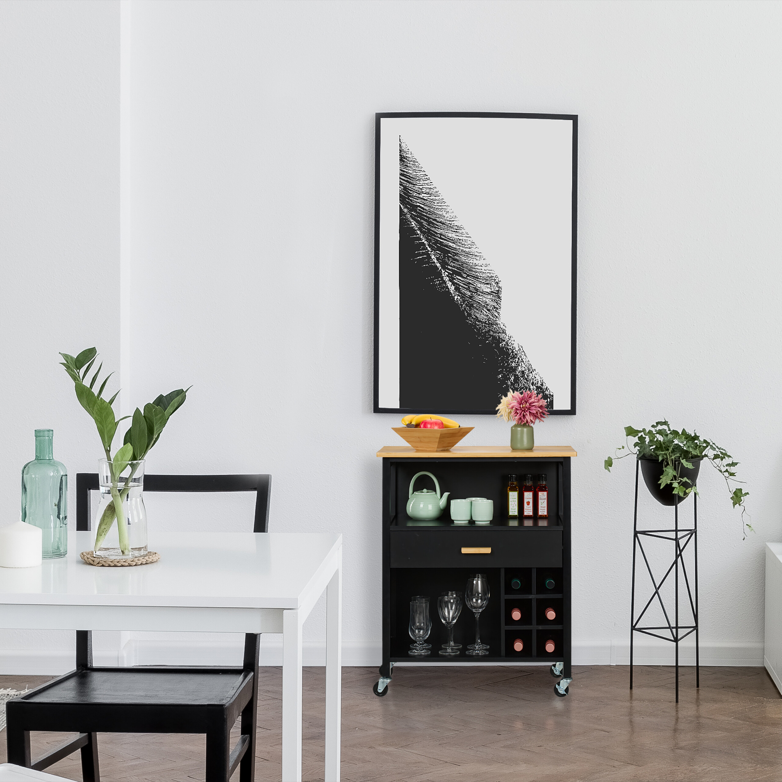 Esszimmer mit weißem Tisch, schwarzem Stuhl, Barwagen, großen Rahmen und Pflanzen auf dem Parkettboden.